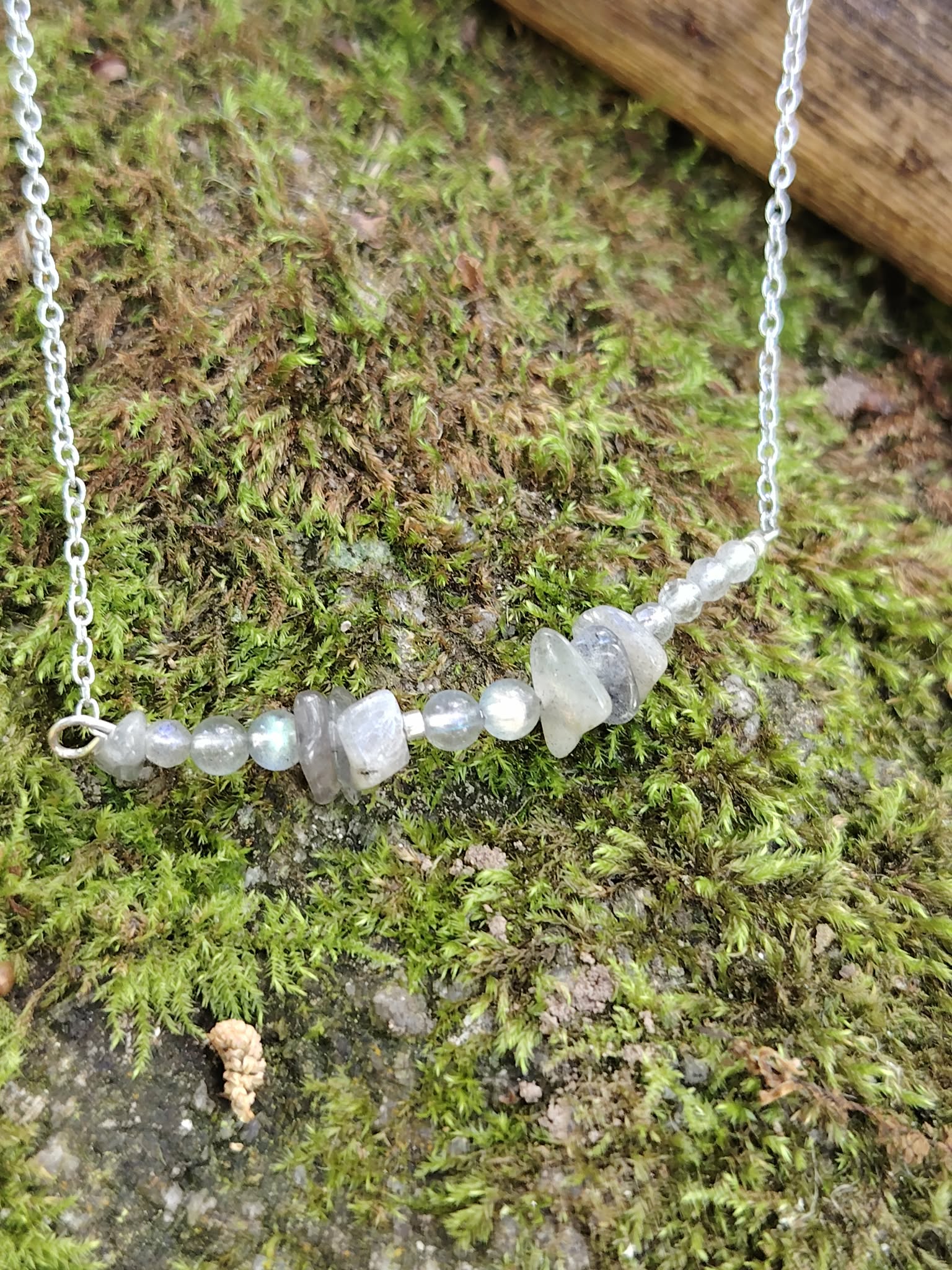 Gros plan sur les pierres de Labradorite du collier, nuances translucides et éclats bleus sur tapis de mousse.