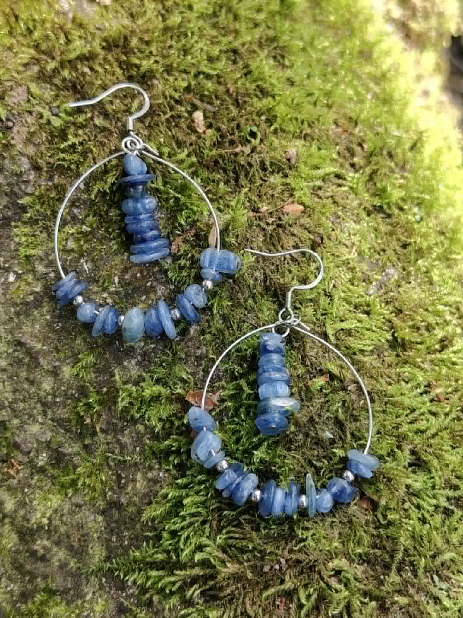 Boucles doreilles créoles cyanite posées sur mousse en forêt, nuances bleues pour apaisement et expression juste.
