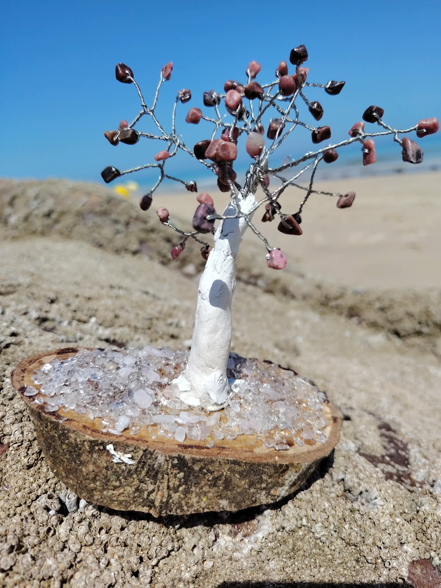 Arbre en rhodonite création Magic Gaïa sur bois et cristal, photographié sur rocher face à la mer en Bretagne.