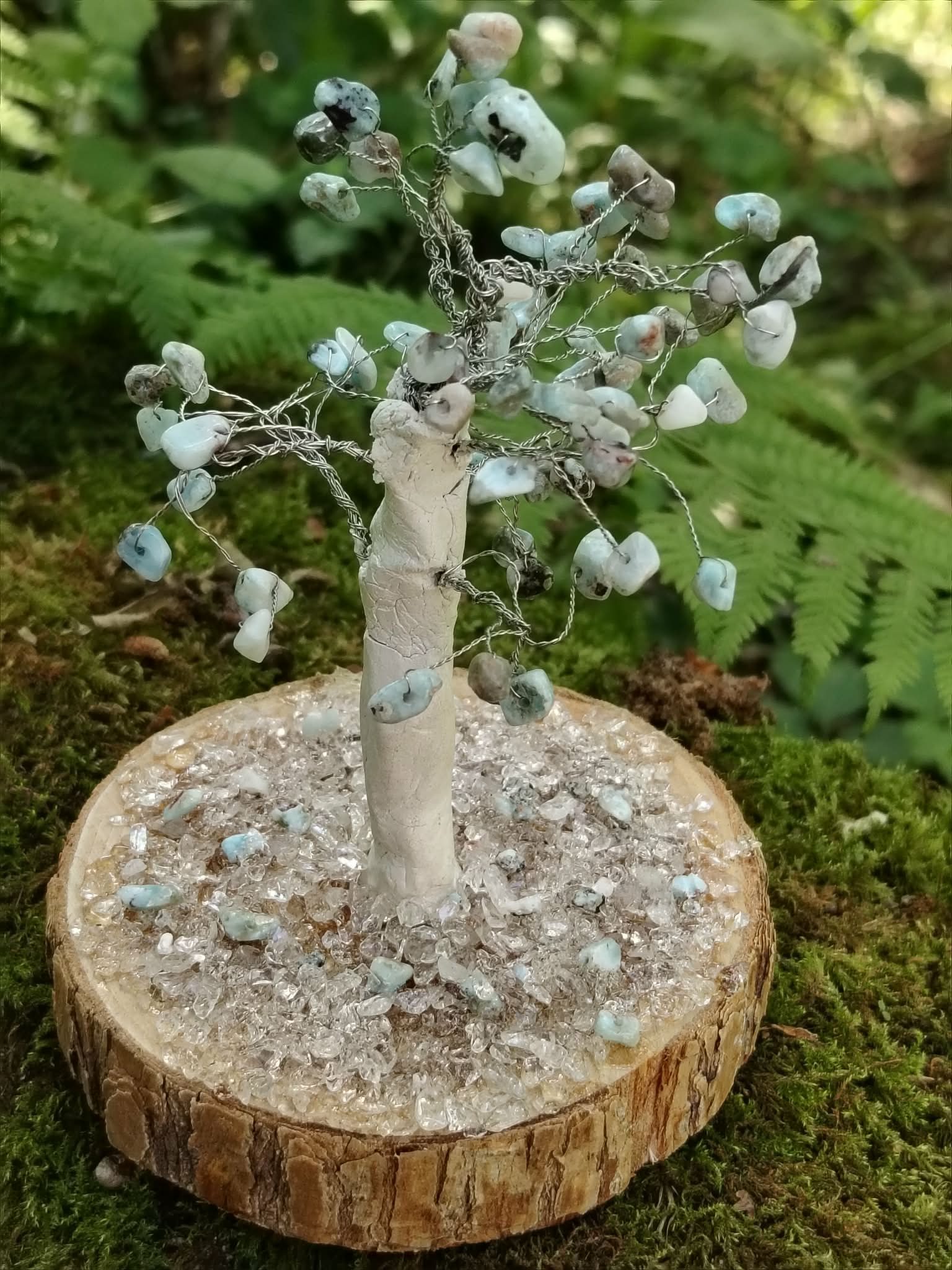 Création Magic Gaïa arbre en larimar sur rondin de bois et éclats de cristal, photographié en forêt parmi la mousse et les fougères.