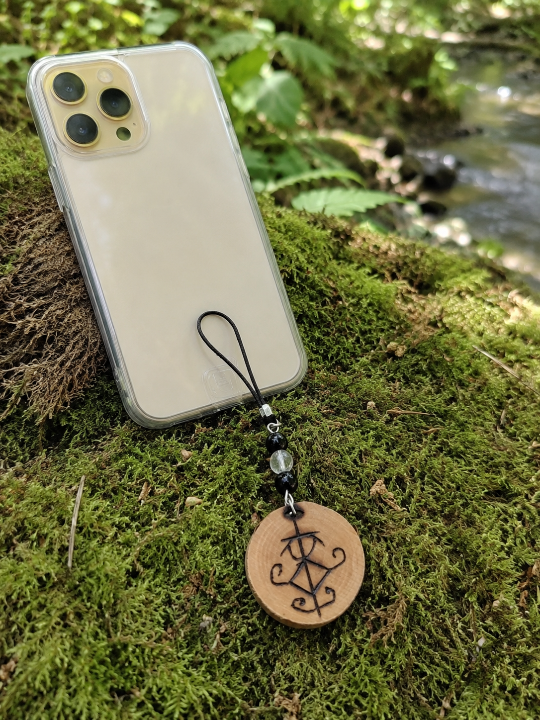 Smartphone avec talisman Magic Gaïa suspendu, bois naturel pyrogravé et pierres associées à l’ancrage protecteur.