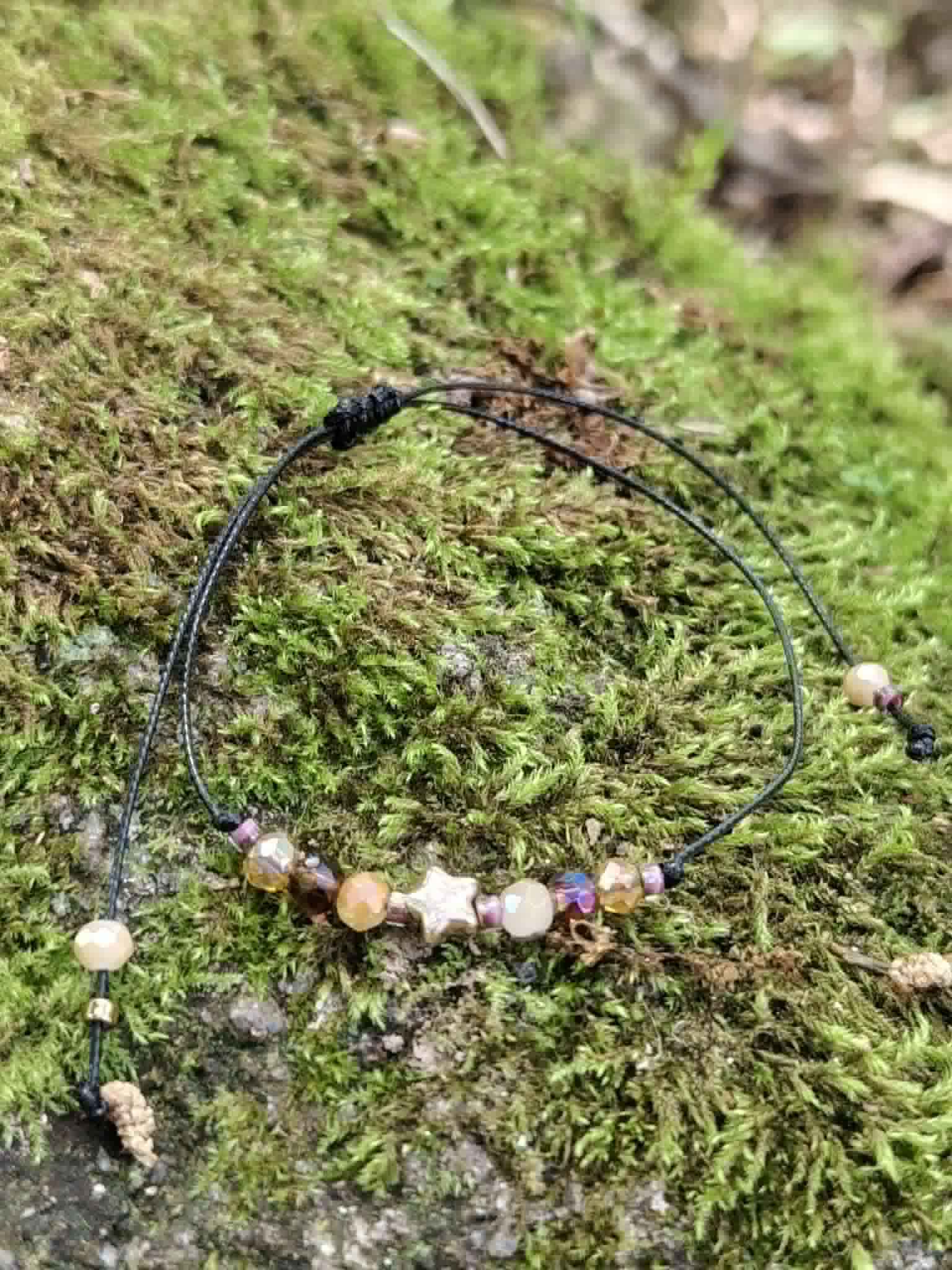 Bracelet réglable avec breloque étoile dorée, perles facettées chaleureuses et cordon noir noué pour un style céleste discret.