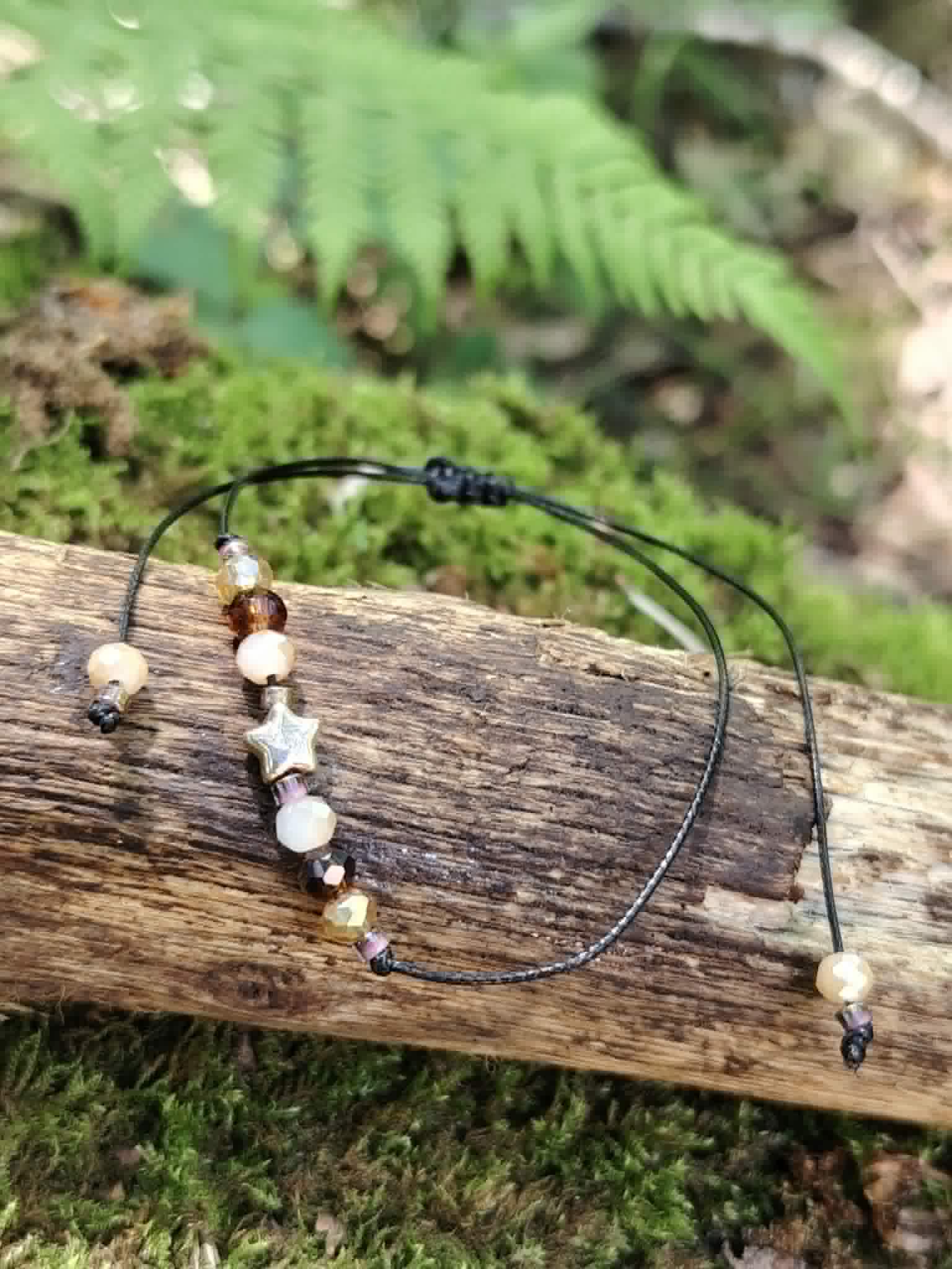 Bracelet cordon noir avec étoile dorée et perles facettées crème, ambrées et rosées, présenté à plat avec ses liens réglables.
