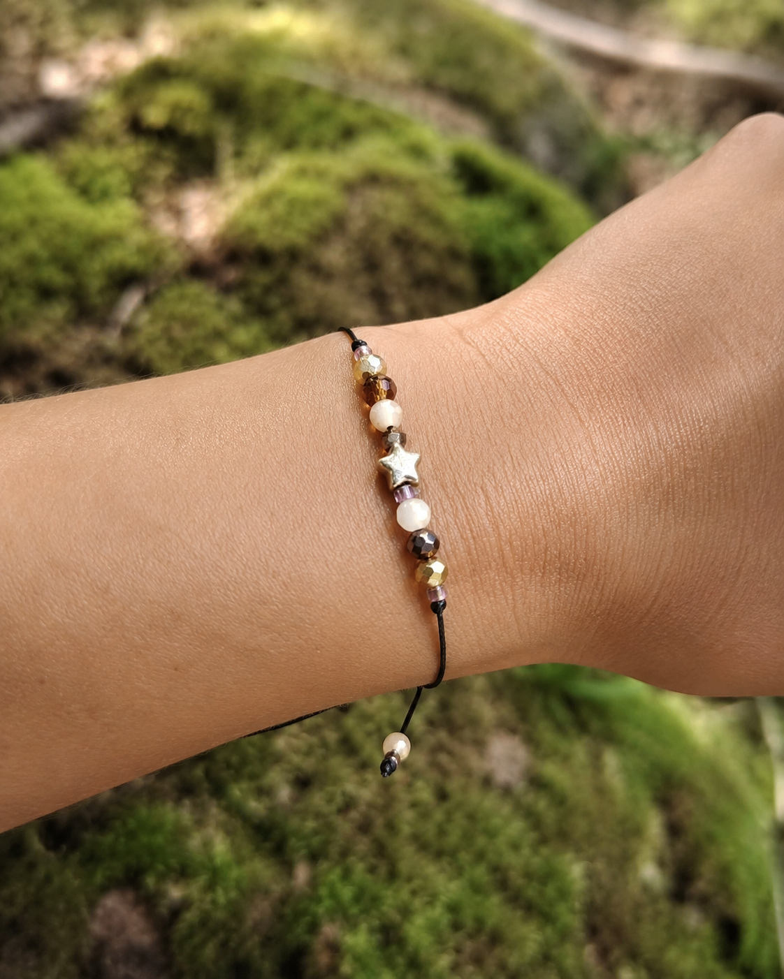 Bracelet étoile dorée porté au poignet en lumière naturelle, cordon noir ajustable et petites perles lumineuses aux tons doux.