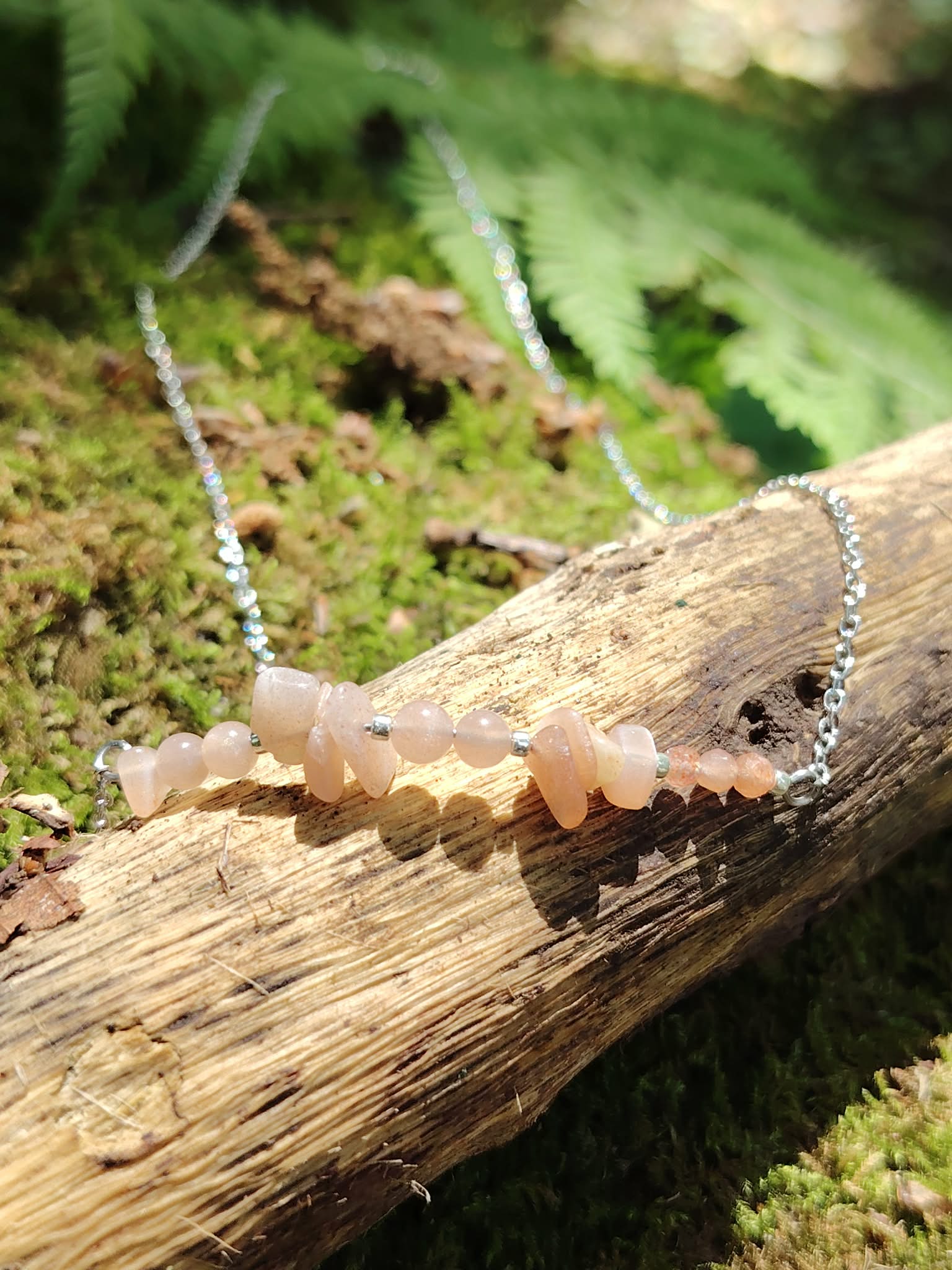 Collier pierre de soleil création Magic Gaïa posé sur branche en forêt, mousse verte, fougères, joie, vitalité et confiance.