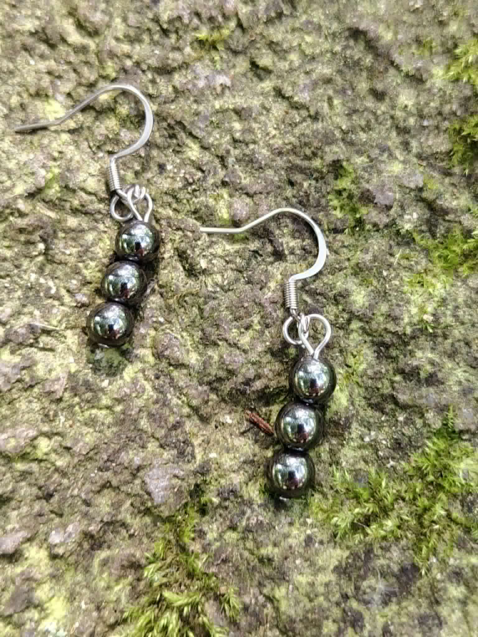 Boucles d’oreilles hématite création Magic Gaïa sur écorce avec mousse verte, reflets brillants, ancrage profond.