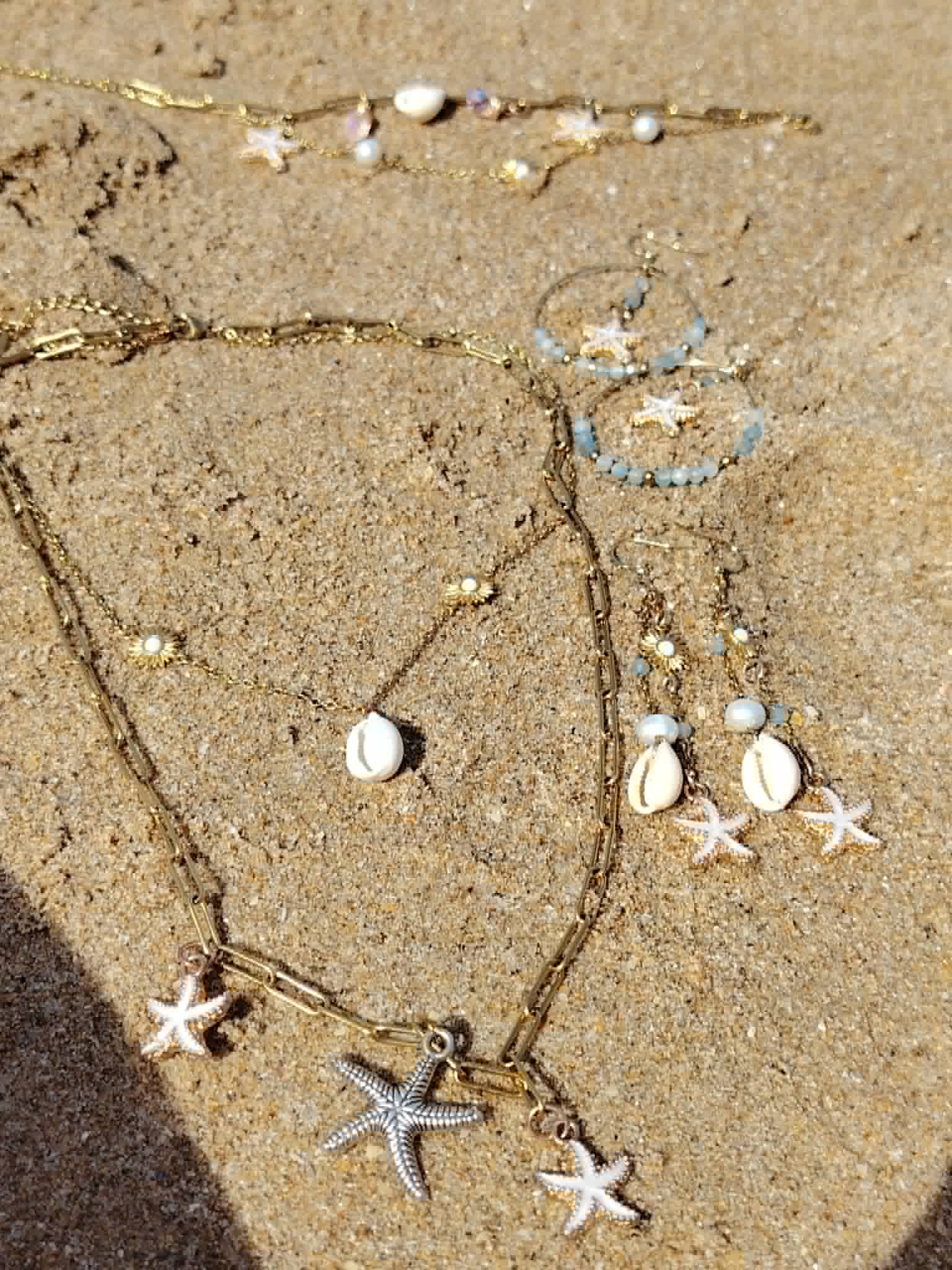 Collier double rang étoiles de mer, bracelet et boucles d’oreilles dorés sur le sable en Vendée