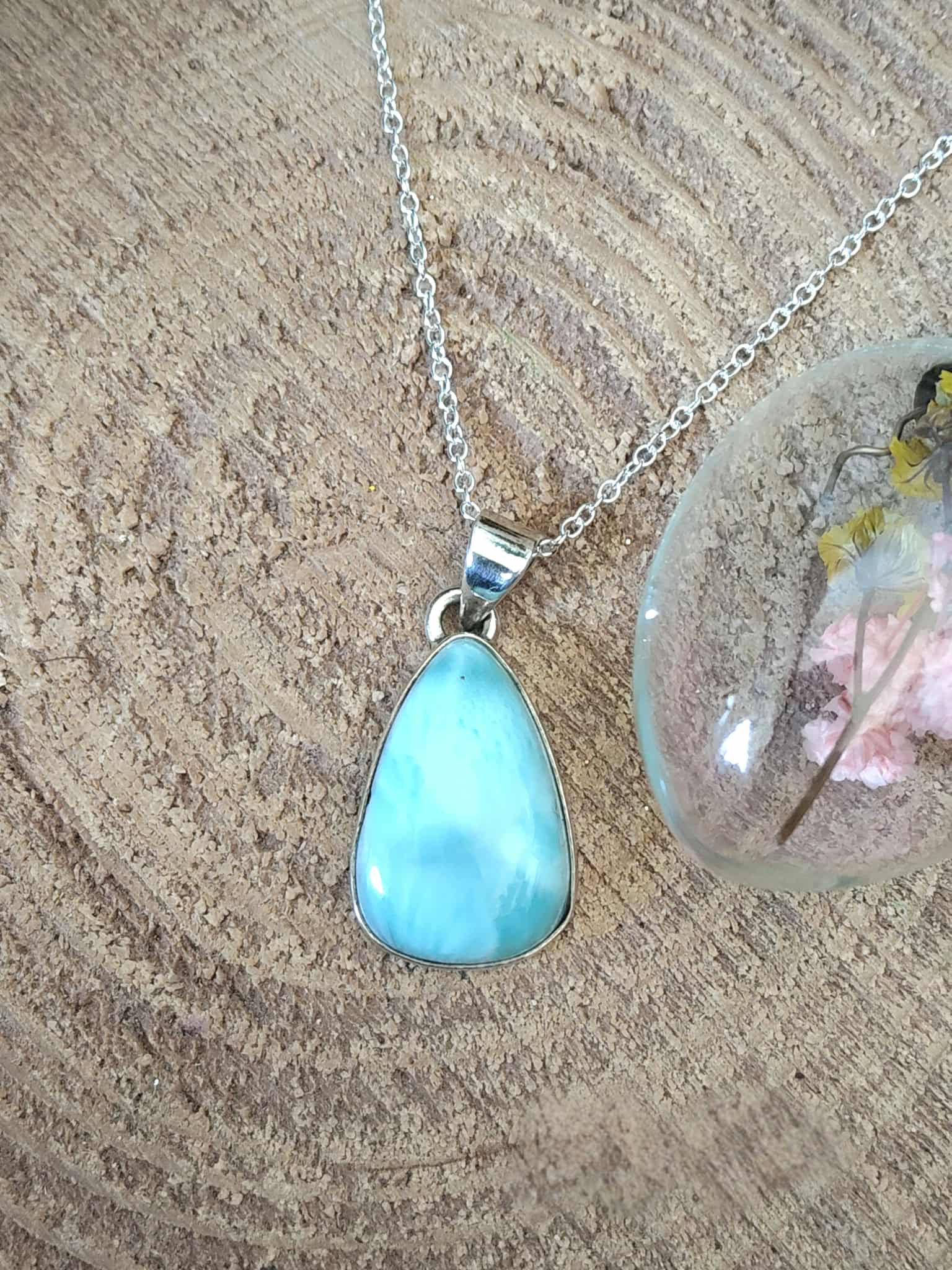 Pendentif larimar bleu monté en argent 925 sur fond bois naturel avec résine fleurie, bijou en pierre naturelle évoquant la douceur, la sérénité et la fluidité intérieure.