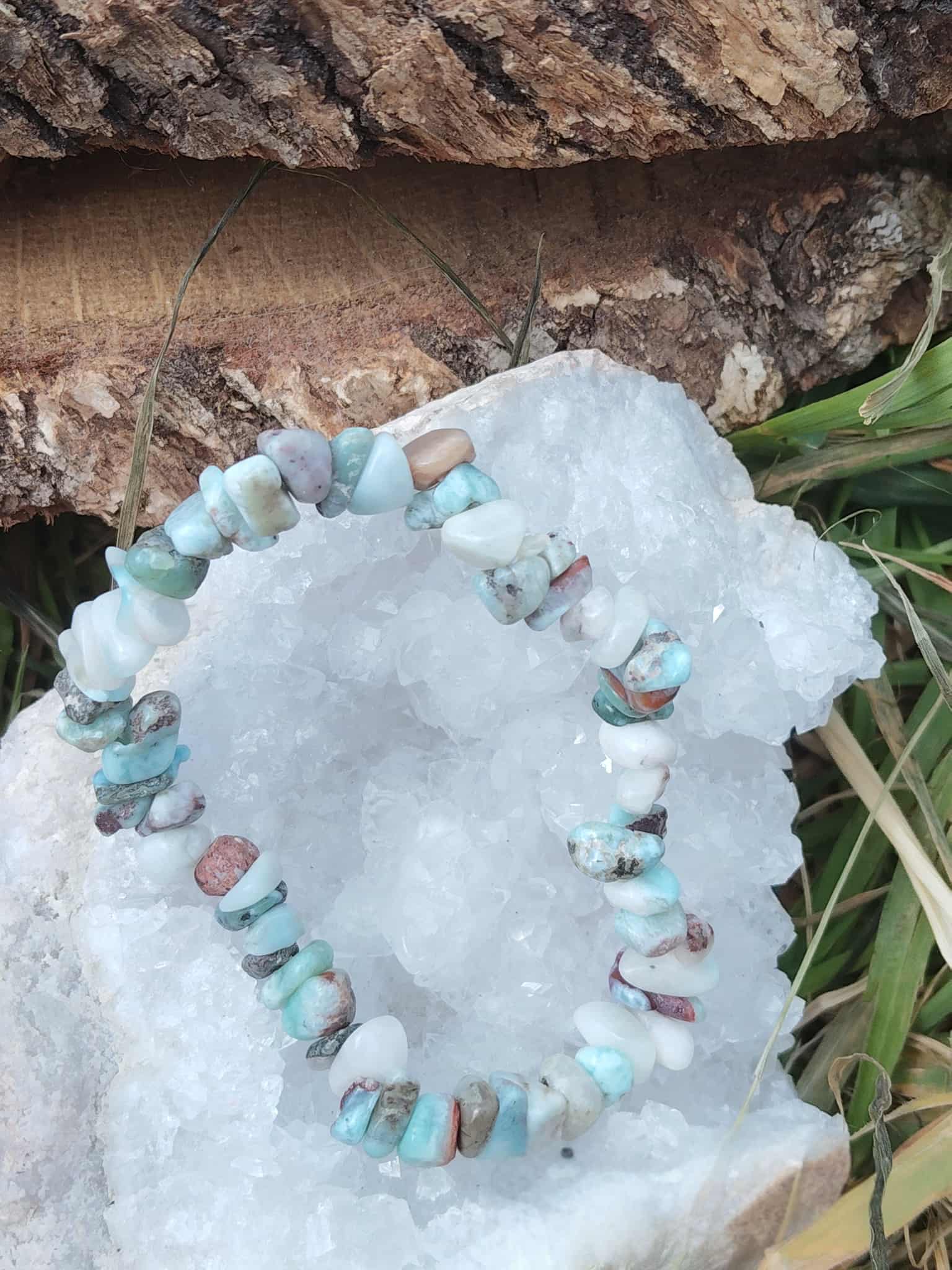 Bracelet larimar baroque posé sur tissu blanc duveteux avec bois brut et feuillage, pierres bleu ciel marbrées pour réconfort affectif et détente mentale