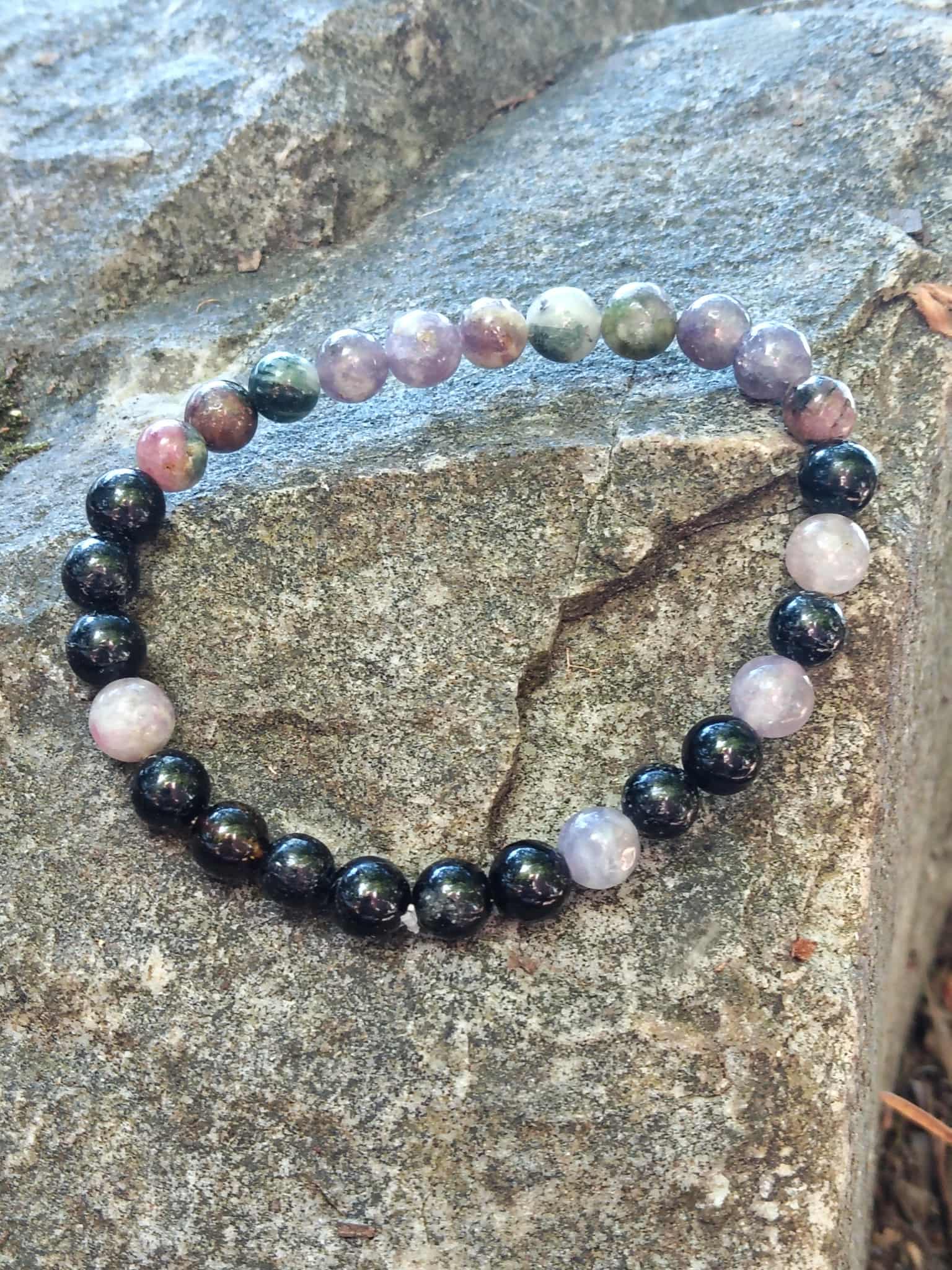 Bracelet en tourmaline multicolore posé à plat sur rocher, perles pastel et noires en 6 mm pour stabilité et bouclier énergétique