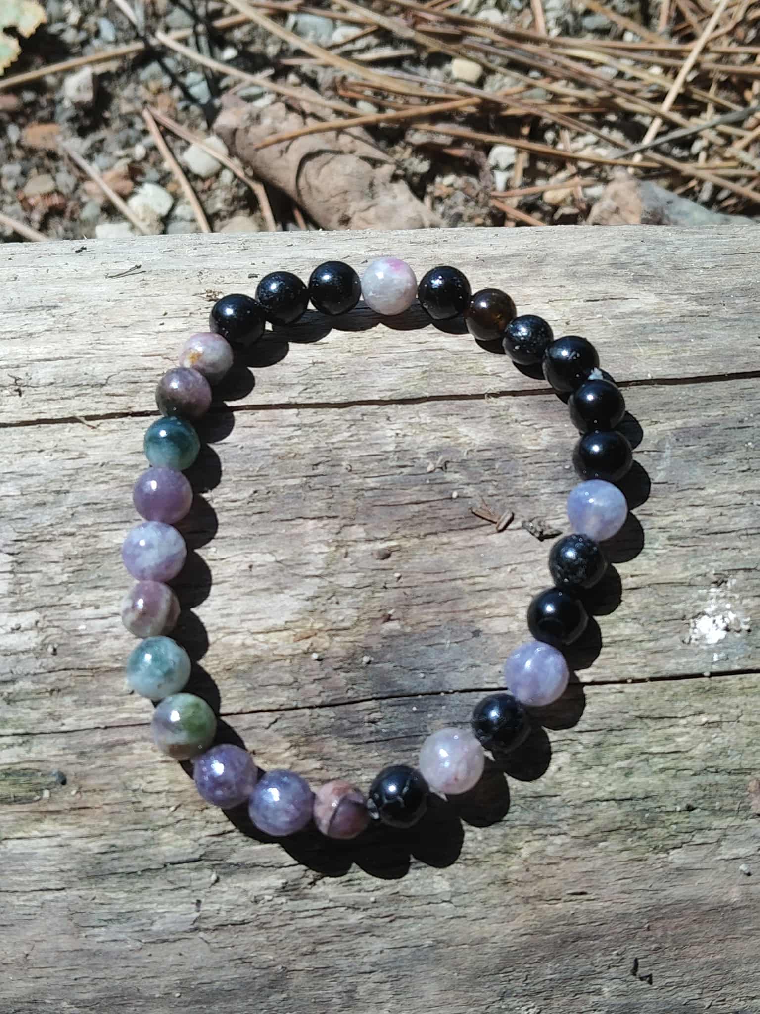 Bracelet tourmaline multicolore 6 mm sur planche de bois en extérieur, perles naturelles violet, vert et noir pour protection et stabilité intérieure