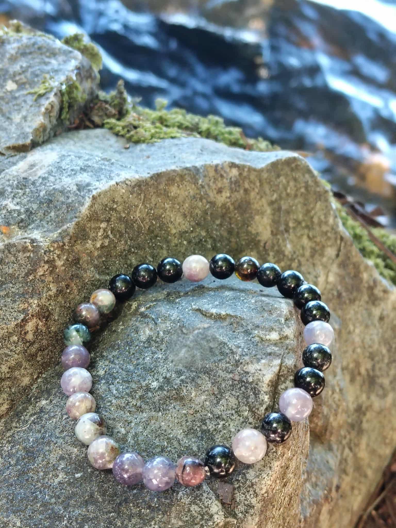 "Bracelet tourmaline multicolore rose, violet et noir sur rocher près de l’eau, pierre naturelle liée au courage et à la protection