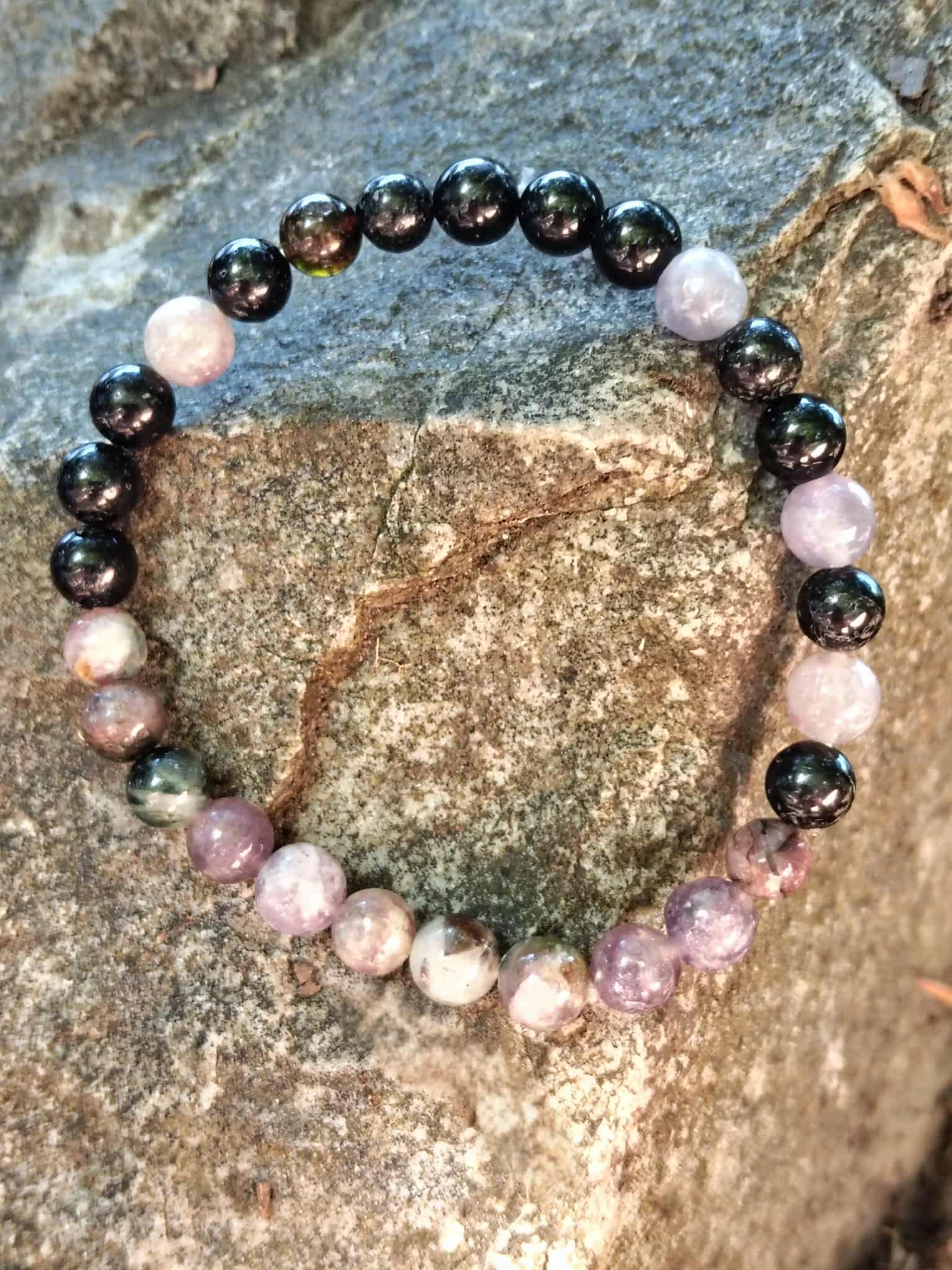Bracelet tourmaline multicolore sur rocher en lumière naturelle, perles rose-violet et noires pour apaisement, ancrage et confiance