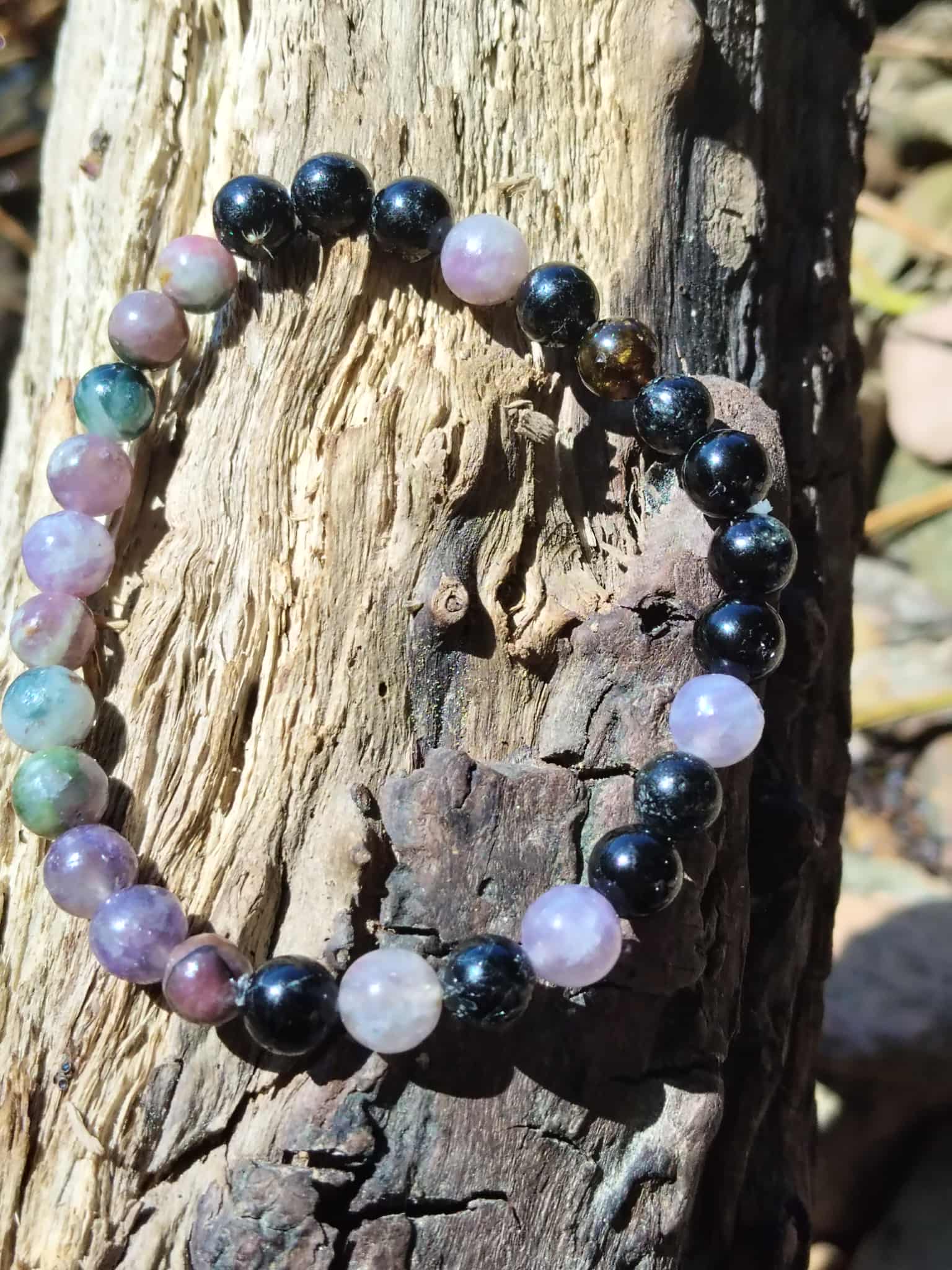 Bracelet en tourmaline multicolore posé sur bois flotté, perles roses, violettes, bleutées et noires pour recentrage et force calme