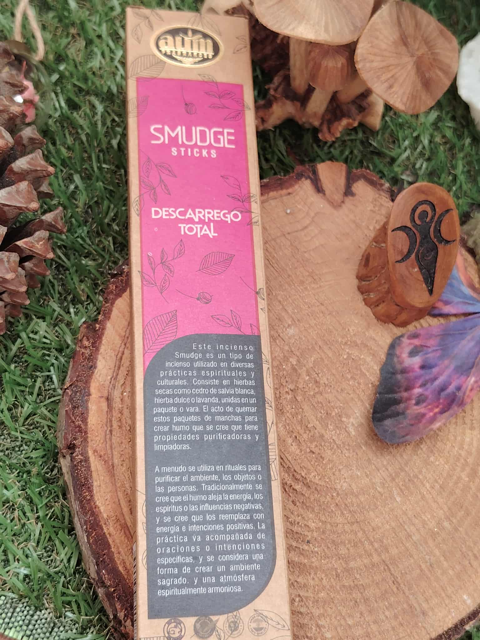 Boîte d’encens Smudge Sticks « Descarga Total » AUM – vue arrière avec notice – posée sur rondins de bois, pelouse et déco symbole Om – encens organique pour rituel de purification/nettoyage énergétique.