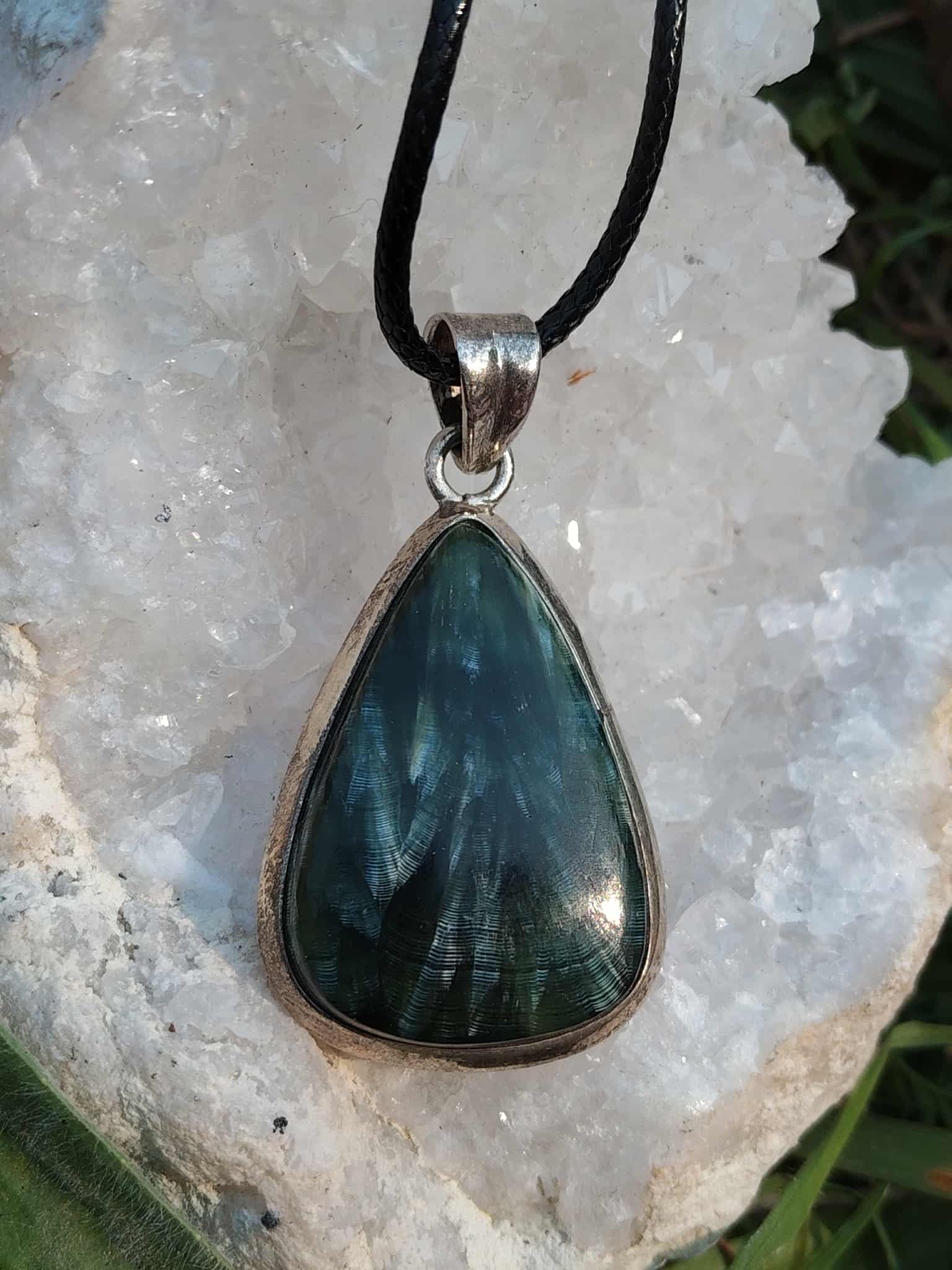 Pendentif séraphinite goutte en argent 925 sur cordon noir, posé sur pierre irisée, bijou en pierre naturelle associé à la douceur émotionnelle, à l’harmonie intérieure et au calme du cœur.