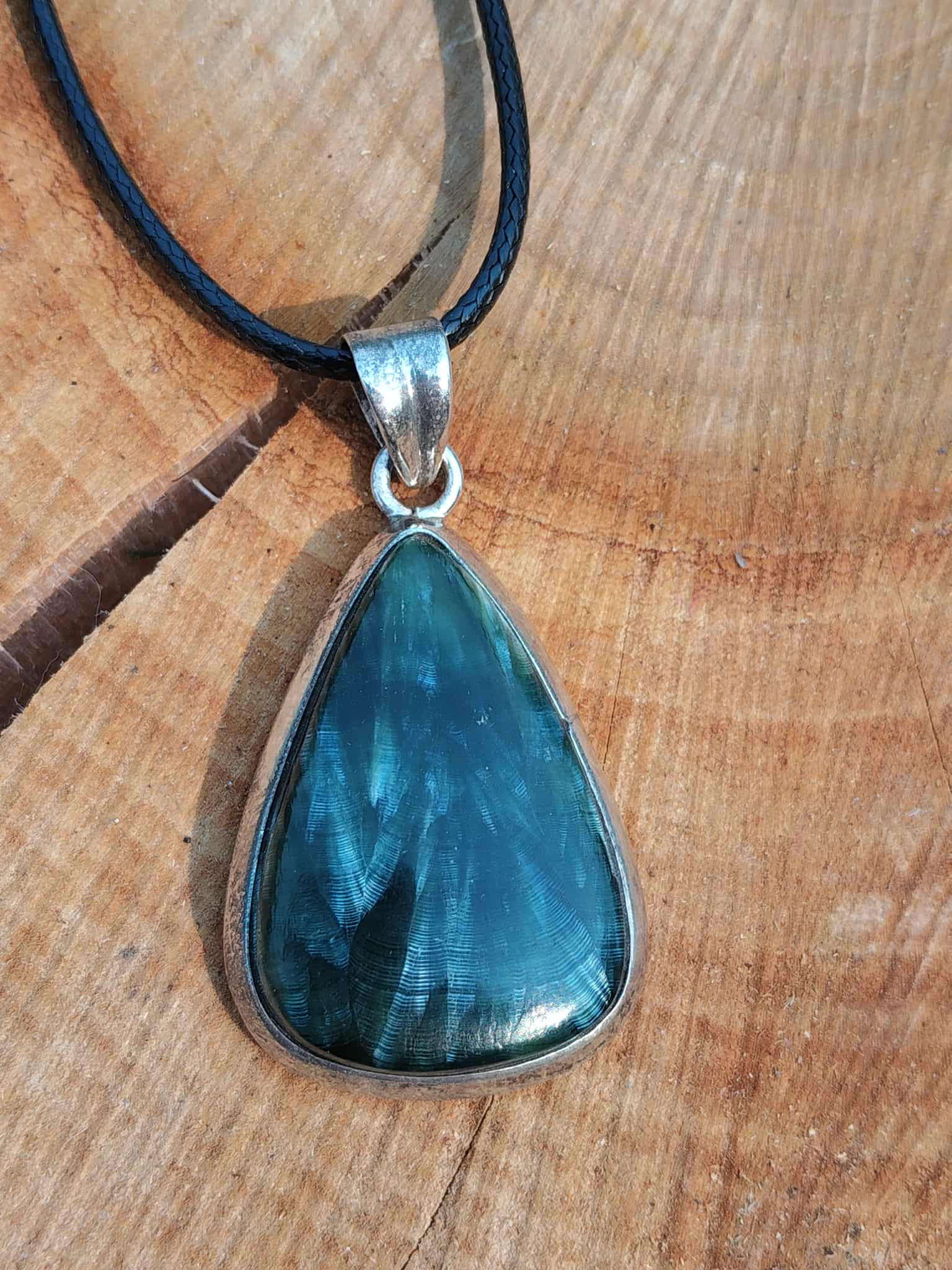 Bijou en séraphinite naturelle cabochon poire avec monture argent 925 sur fond bois, pierre naturelle associée au réconfort, à la stabilité émotionnelle et à la douceur intérieure.