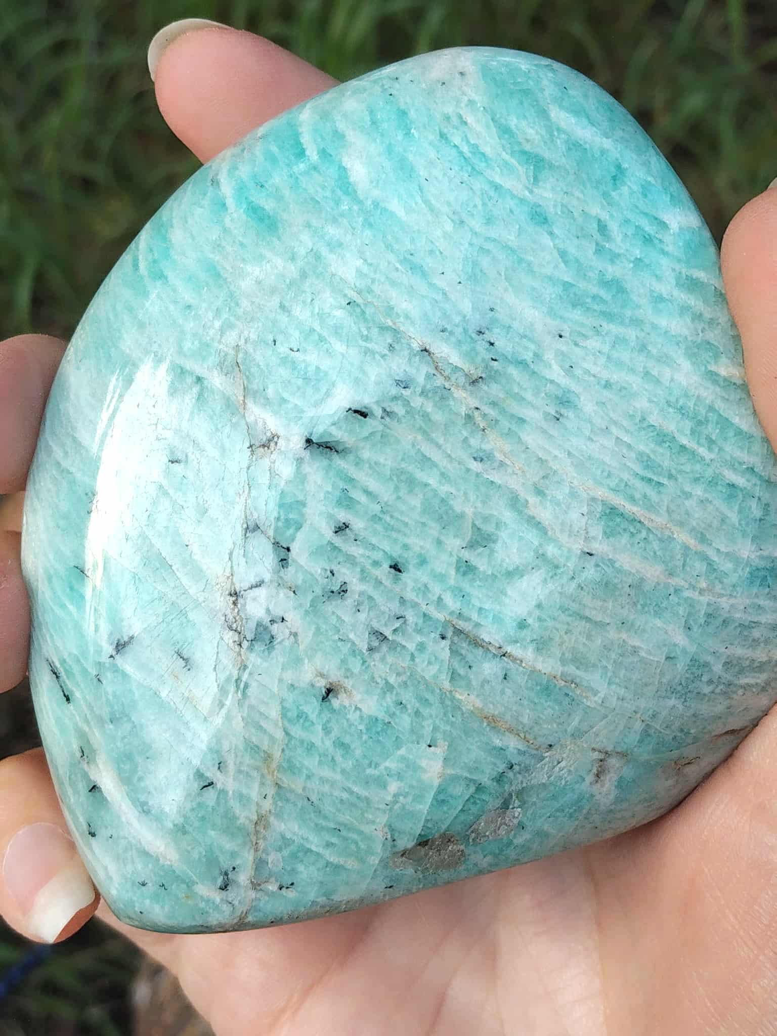 Forme libre Amazonite tenue en main, gros plan sur les marbrures bleu-vert et les inclusions naturelles de la pierre.