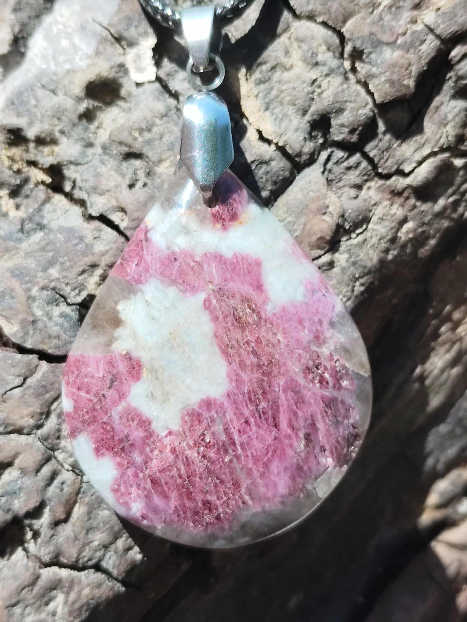 Gros plan sur pendentif goutte en tourmaline rose avec bélière en acier inoxydable, photographié sur écorce, bijou en pierre naturelle évoquant la délicatesse, la paix émotionnelle et le réconfort.