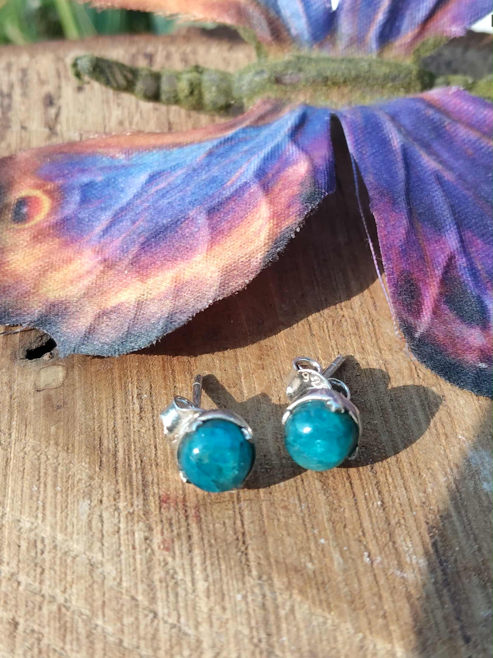 Boucles d’oreilles apatite bleue cabochons ronds en argent 925, posées sur planche de bois avec papillon décoratif à côté — stimule la créativité et l’inspiration.