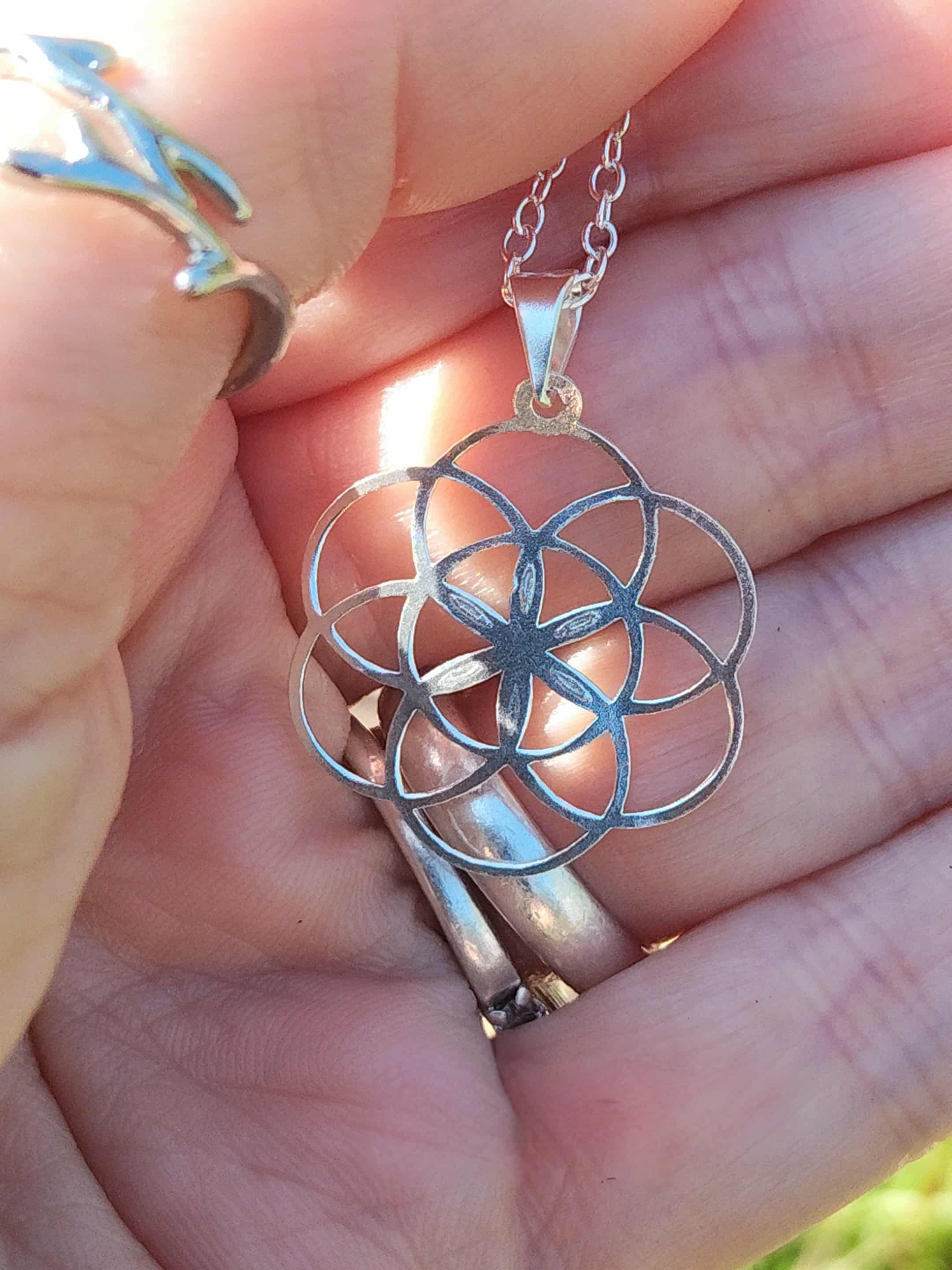 Pendentif graine de vie en argent 925 tenu dans la main, motif de géométrie sacrée à sept cercles bien visible