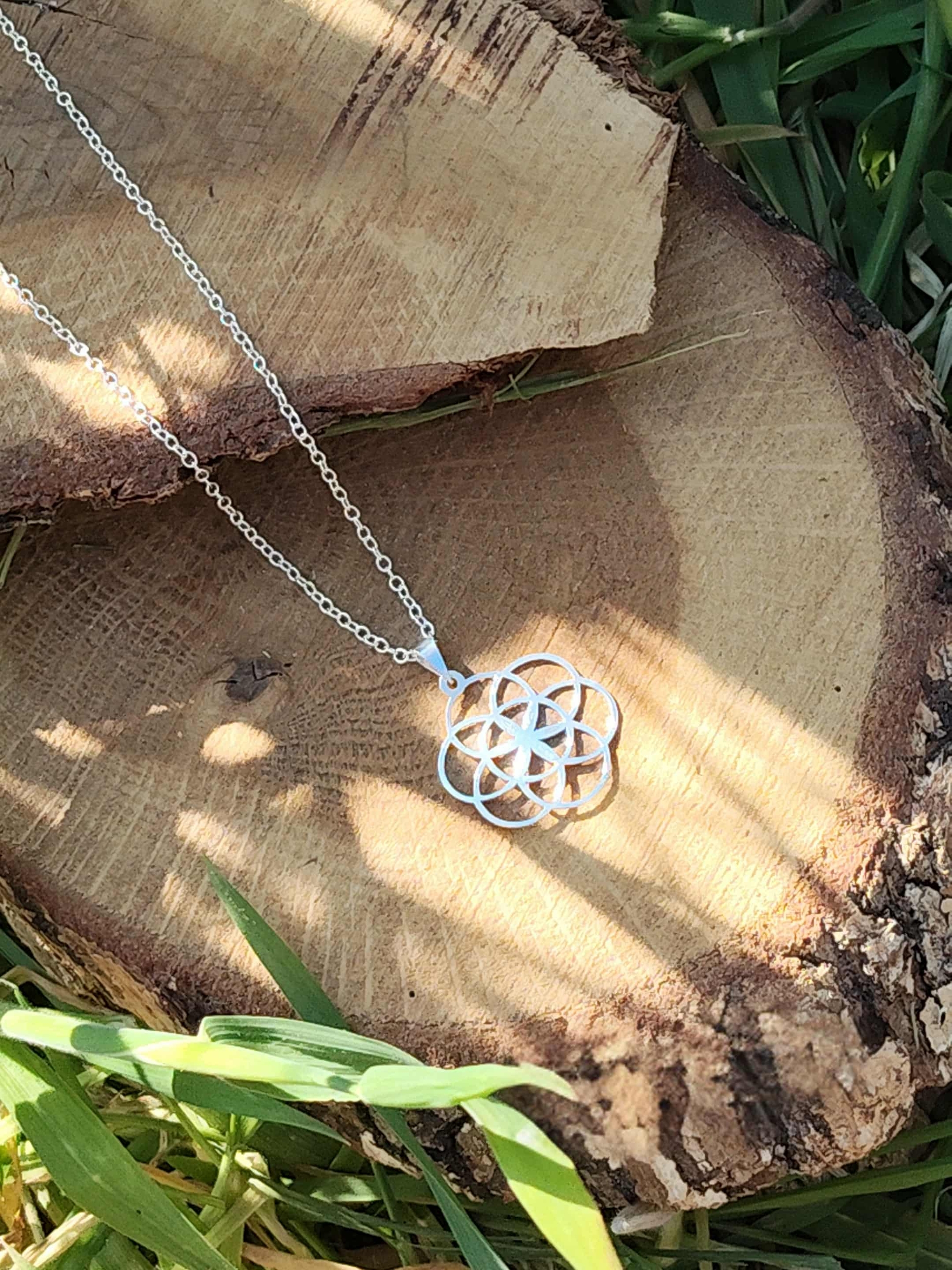 Pendentif graine de vie argenté sur rondin de bois, symbole de géométrie sacrée pour harmonie visuelle et style spirituel
