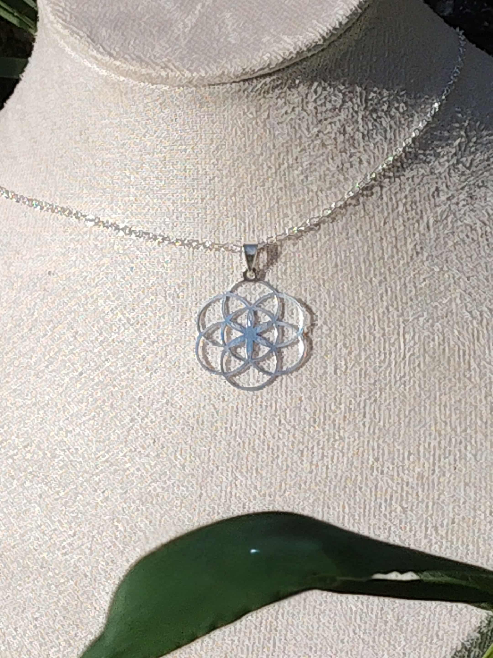 Pendentif graine de vie en argent 925 sur buste mannequin avec chaîne fine et feuille verte au premier plan