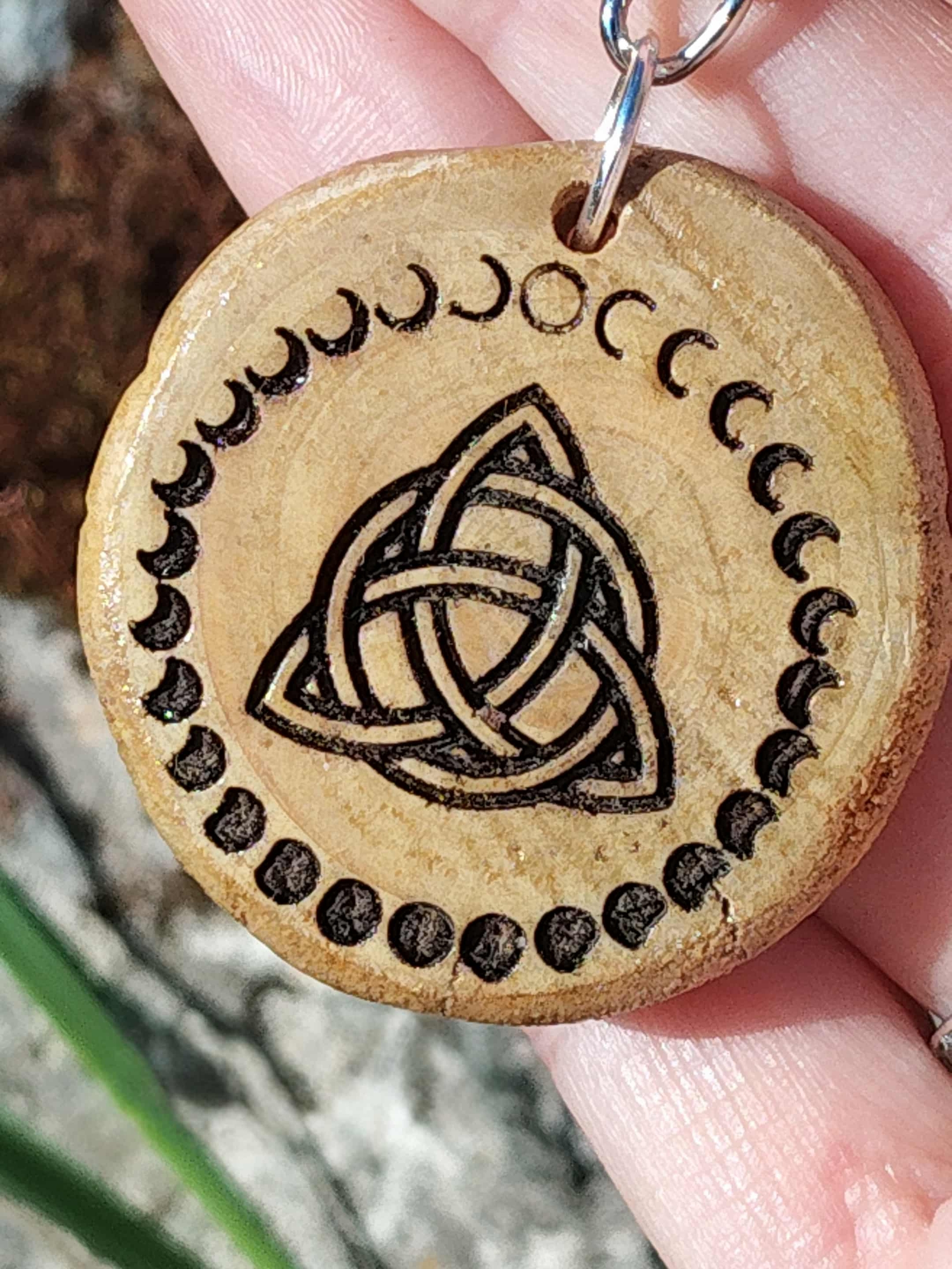 Gros plan porte-clés en bois gravé triquetra celtique et phases de lune, tenu entre les doigts