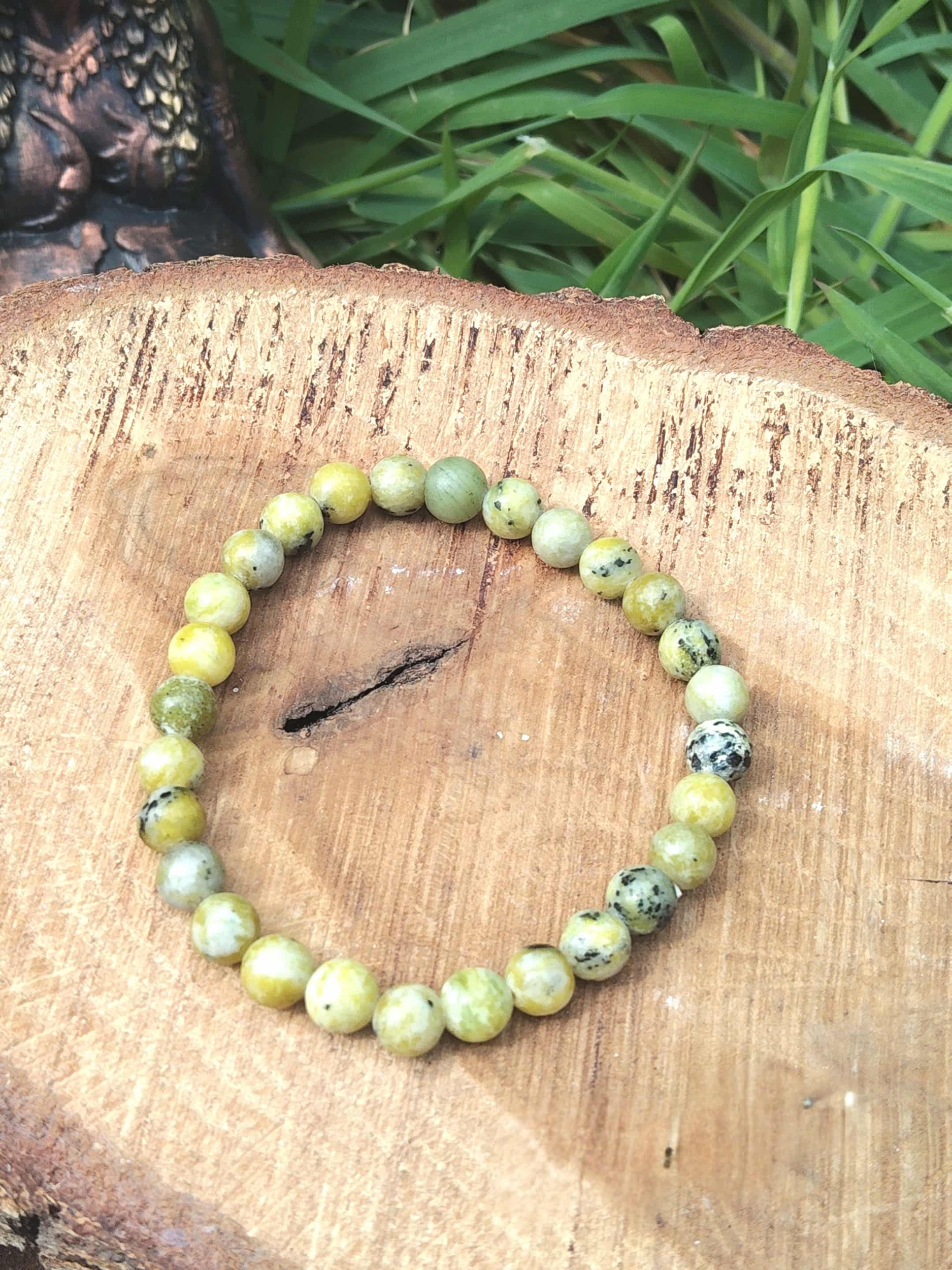 Bijou bracelet serpentine vert-jaune sur tranche de bois, harmonie intérieure et détente émotionnelle.
