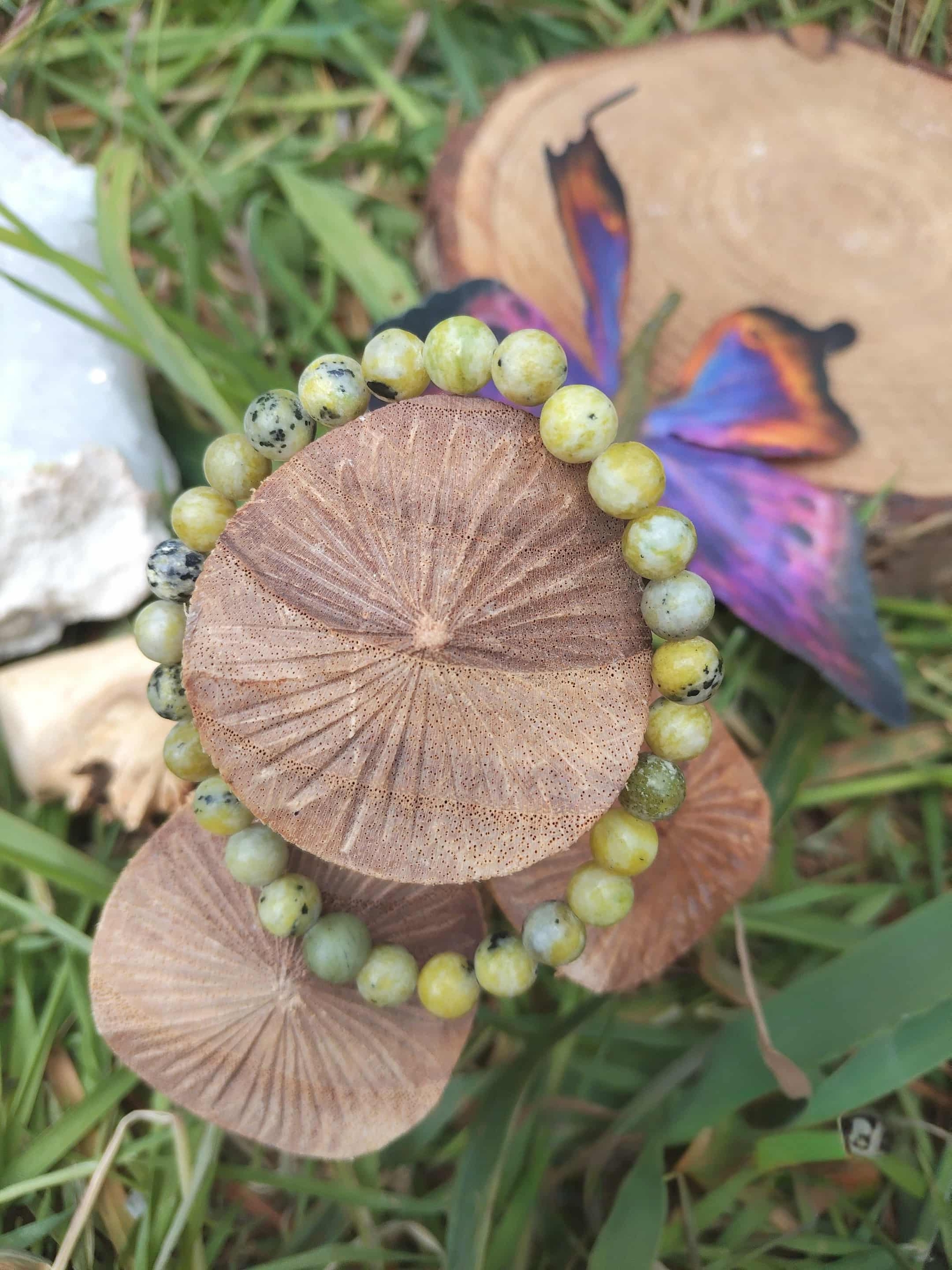 Bracelet serpentine perles 6 mm posé sur rondins, herbes et papillon — lâcher-prise, clarté d’esprit