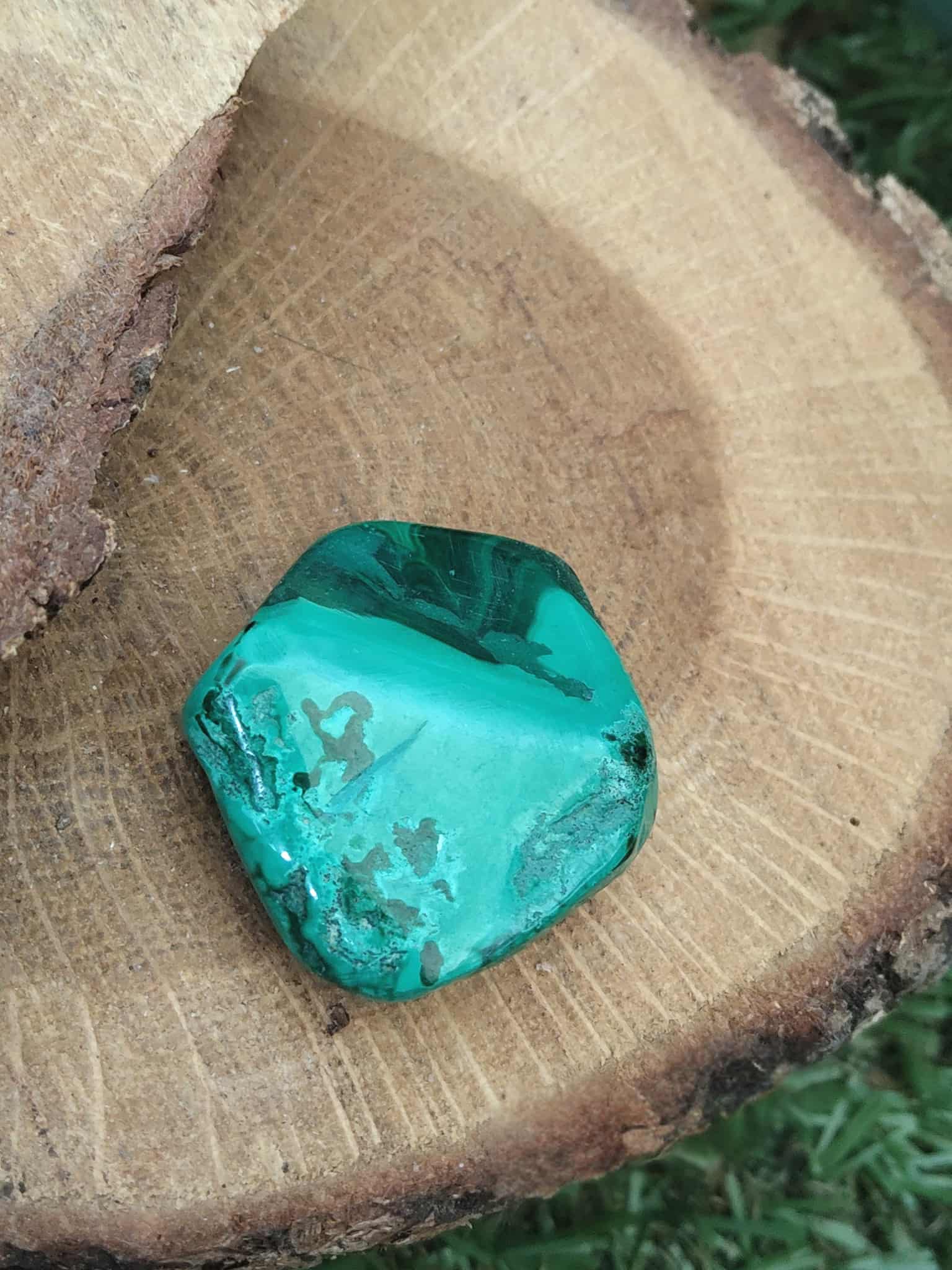 Pierre naturelle malachite à bandes concentriques sur bois ; décor extérieur herbe — transmutation des énergies, clarté émotionnelle