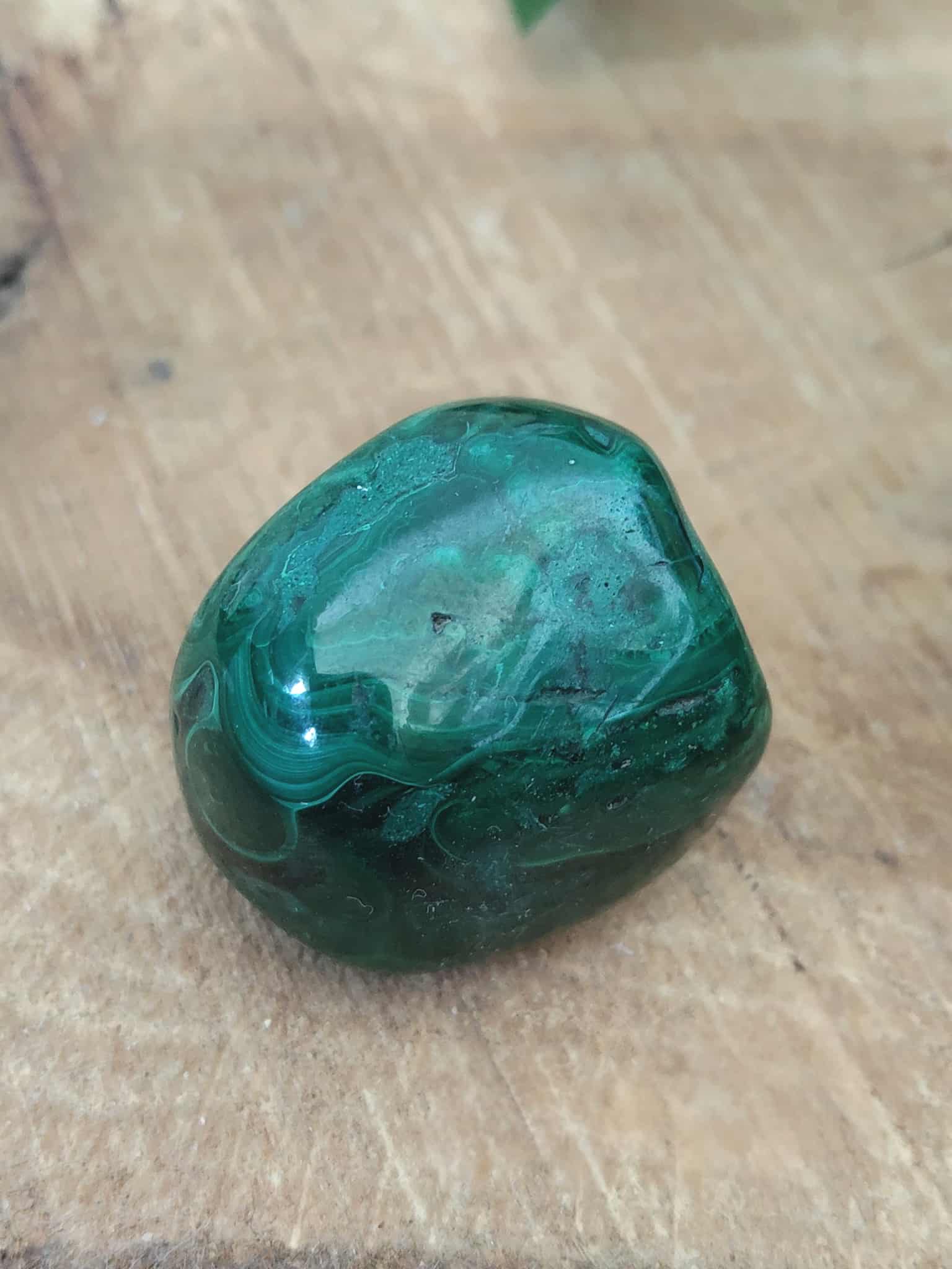 Malachite roulée vert profond sur planche de bois — veines naturelles, protection, transformation, équilibre émotionnel.