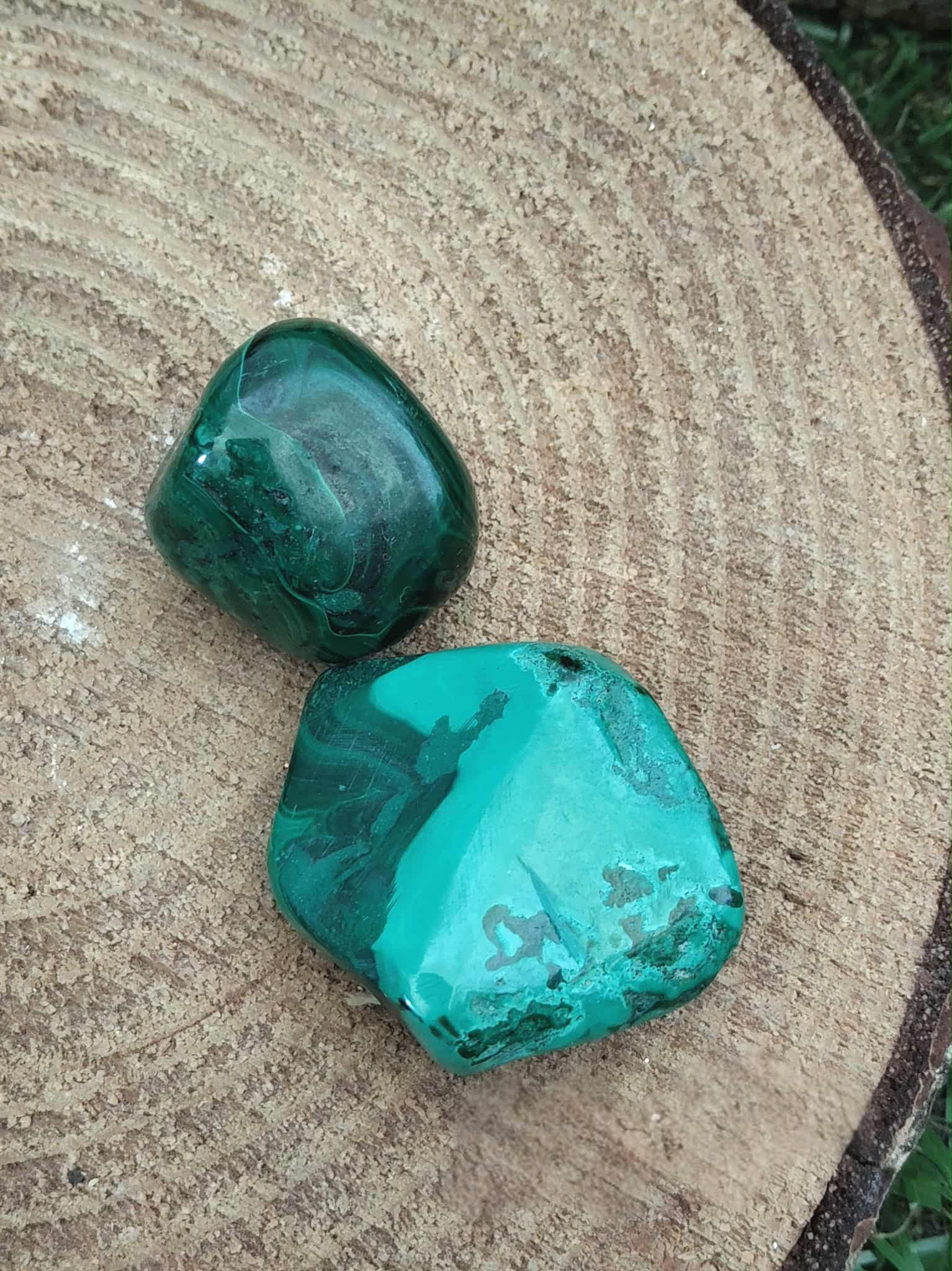 Deux pierres de malachite polies aux veines vertes, posées sur tranche de bois — ancrage doux et harmonie émotionnelle