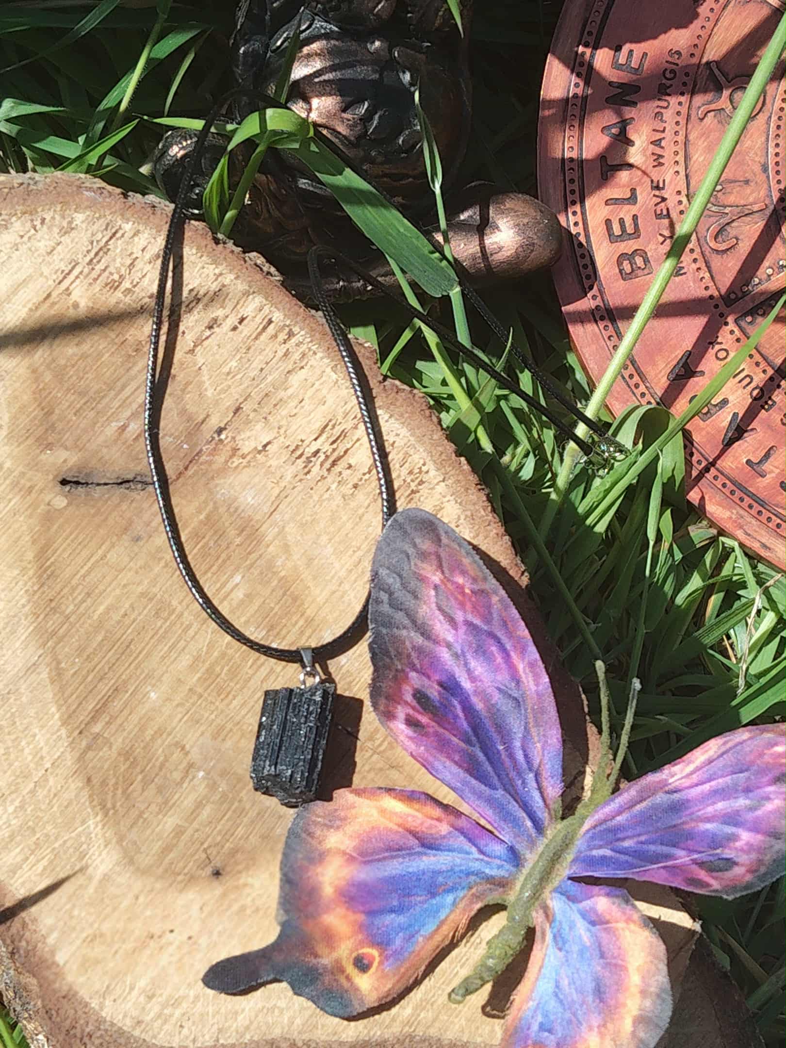 Tourmaline noire brute en pendentif posée sur bois avec papillon illustré et feuillage, bijou en pierre naturelle associé à la protection, au calme du mental et à la présence à soi.