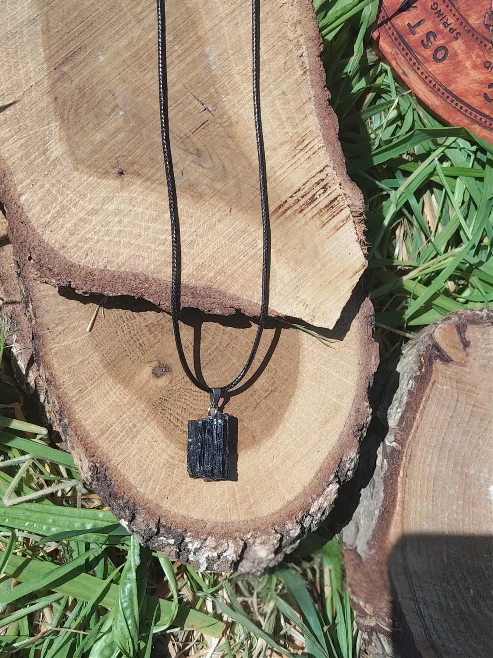 Pendentif en tourmaline noire brute posé sur tranche de bois avec décor végétal, bijou en pierre naturelle évoquant le recentrage, la clarté intérieure et la protection douce.
