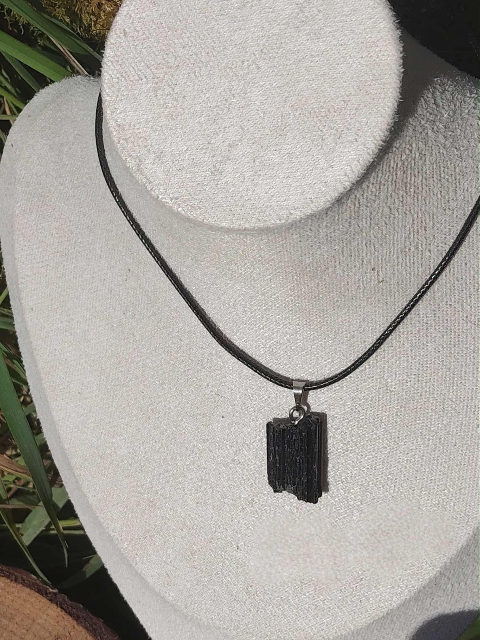Pendentif en tourmaline noire brute sur cordon noir, présenté sur fond clair, bijou en pierre naturelle évoquant la force intérieure, l’équilibre et l’ancrage profond.