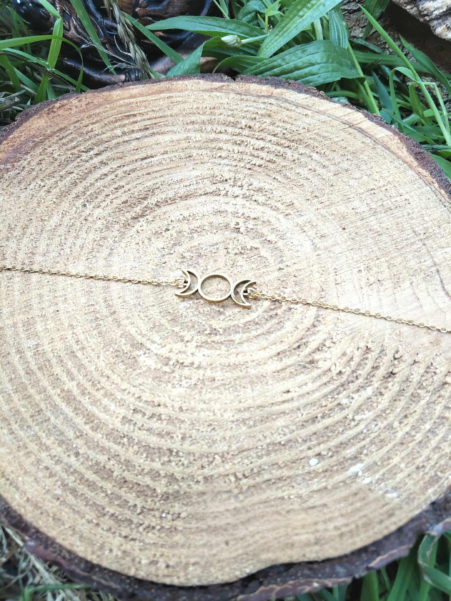 Bracelet Triple Lune doré sur rondin de bois avec herbe autour, bijou ésotérique en acier inoxydable