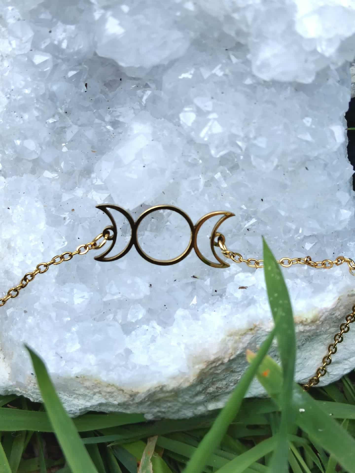 Bracelet Triple Lune en acier inoxydable doré sur géode blanche et herbes vertes, bijou lunaire raffiné.
