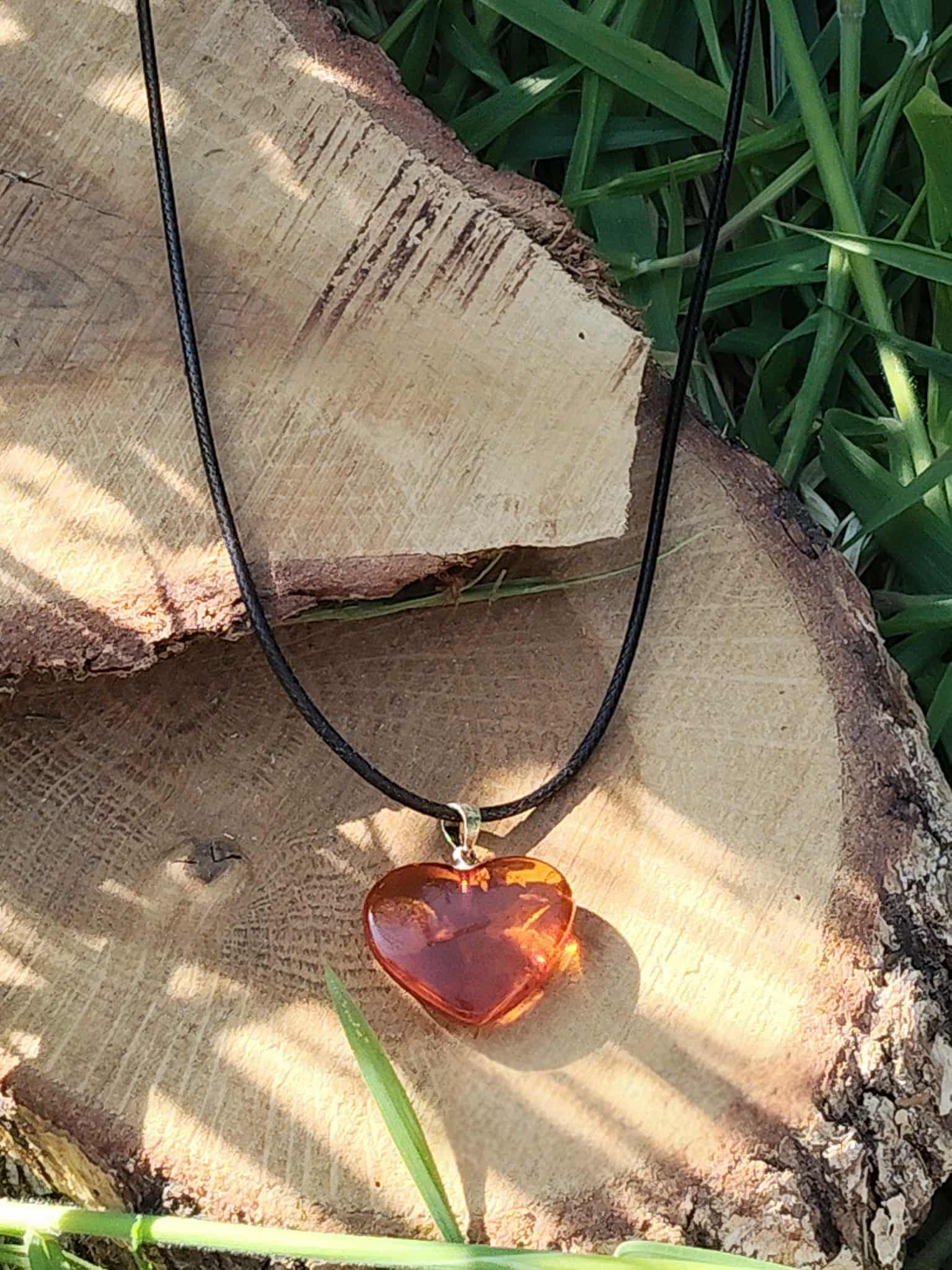 Pendentif cœur en ambre naturel sur bois en lumière solaire, pierre chaleureuse associée à la vitalité, à la joie douce et à l’apaisement émotionnel.