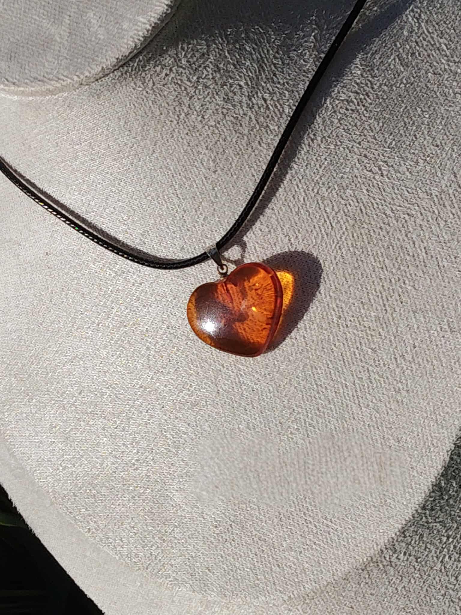 Pendentif cœur en ambre naturel sur cordon noir porté au cou, bijou aux reflets miel associé à l’élégance, à la chaleur intérieure et à la douceur émotionnelle.