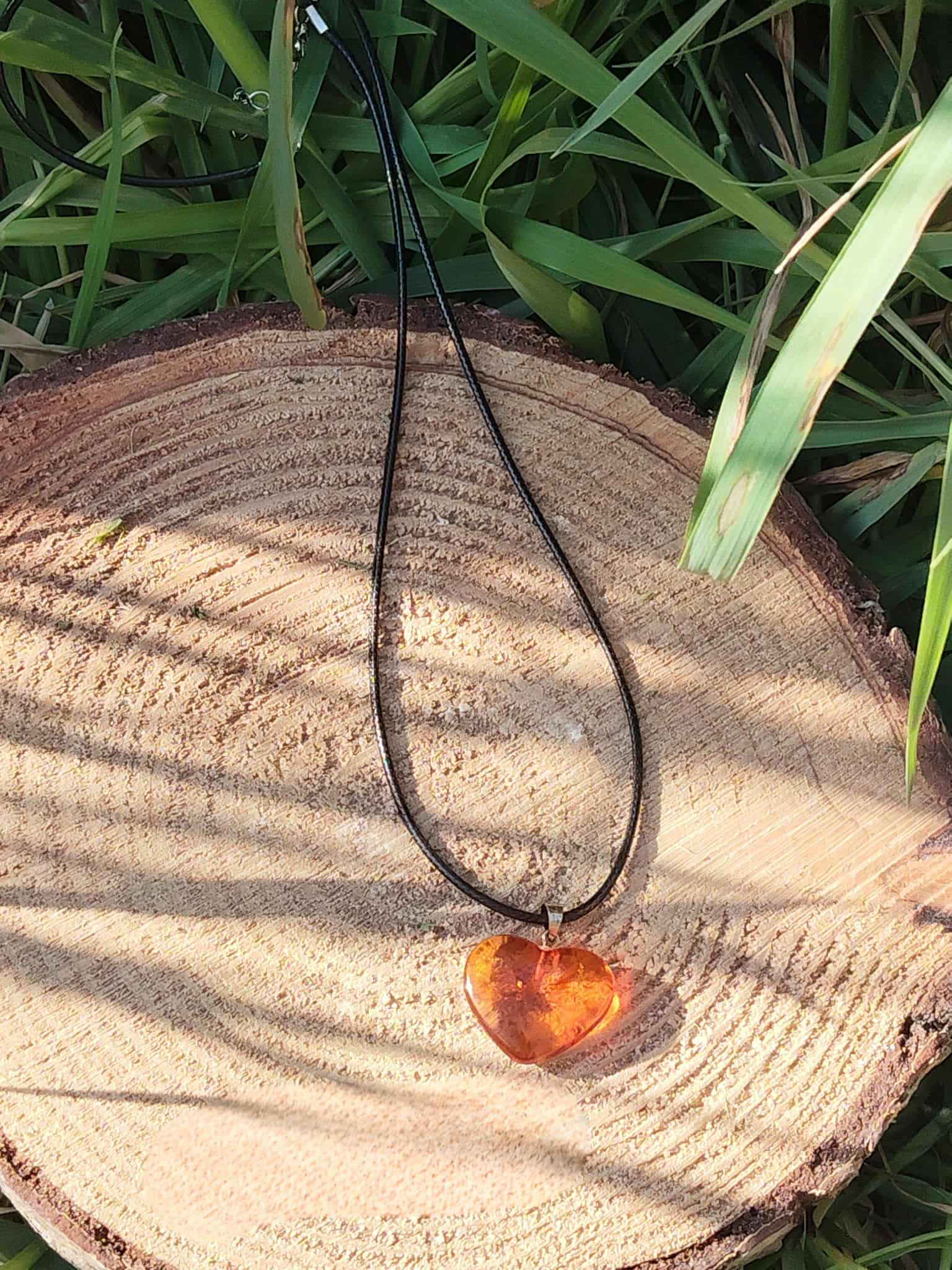 Pendentif cœur d’ambre posé sur rondin de bois, bijou aux tons miel associé à la sérénité, à la stabilité intérieure et à la chaleur réconfortante.