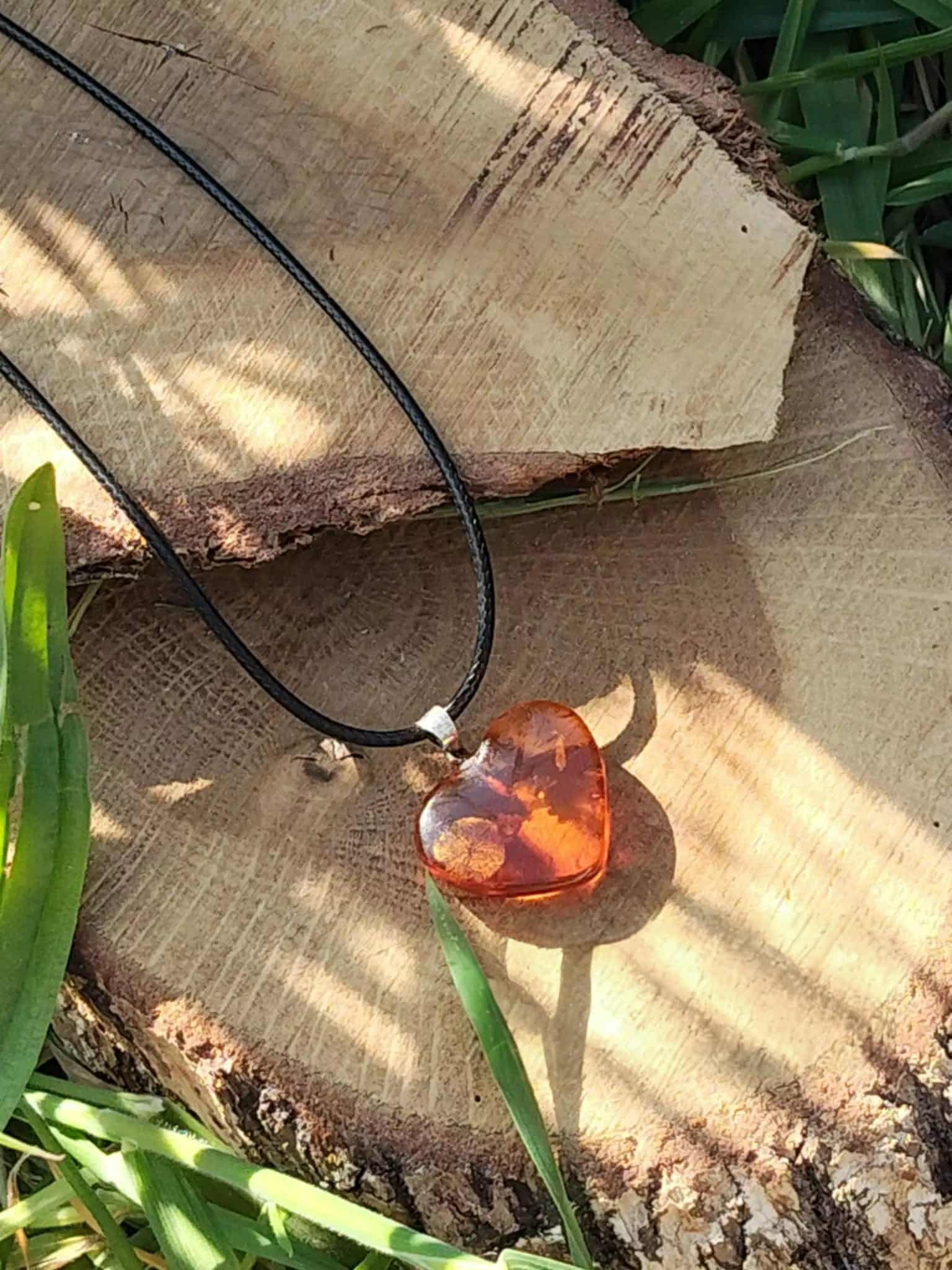 Pendentif cœur en ambre naturel parmi des feuilles vertes au soleil, bijou aux teintes chaudes associé à la douceur, au réconfort et à la lumière intérieure.