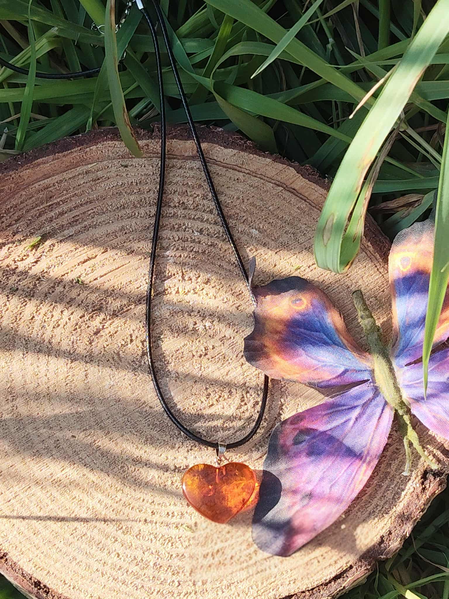 Pendentif cœur en ambre naturel sur bois avec papillon, bijou aux nuances dorées évoquant la confiance, la chaleur du cœur et la lumière apaisante.