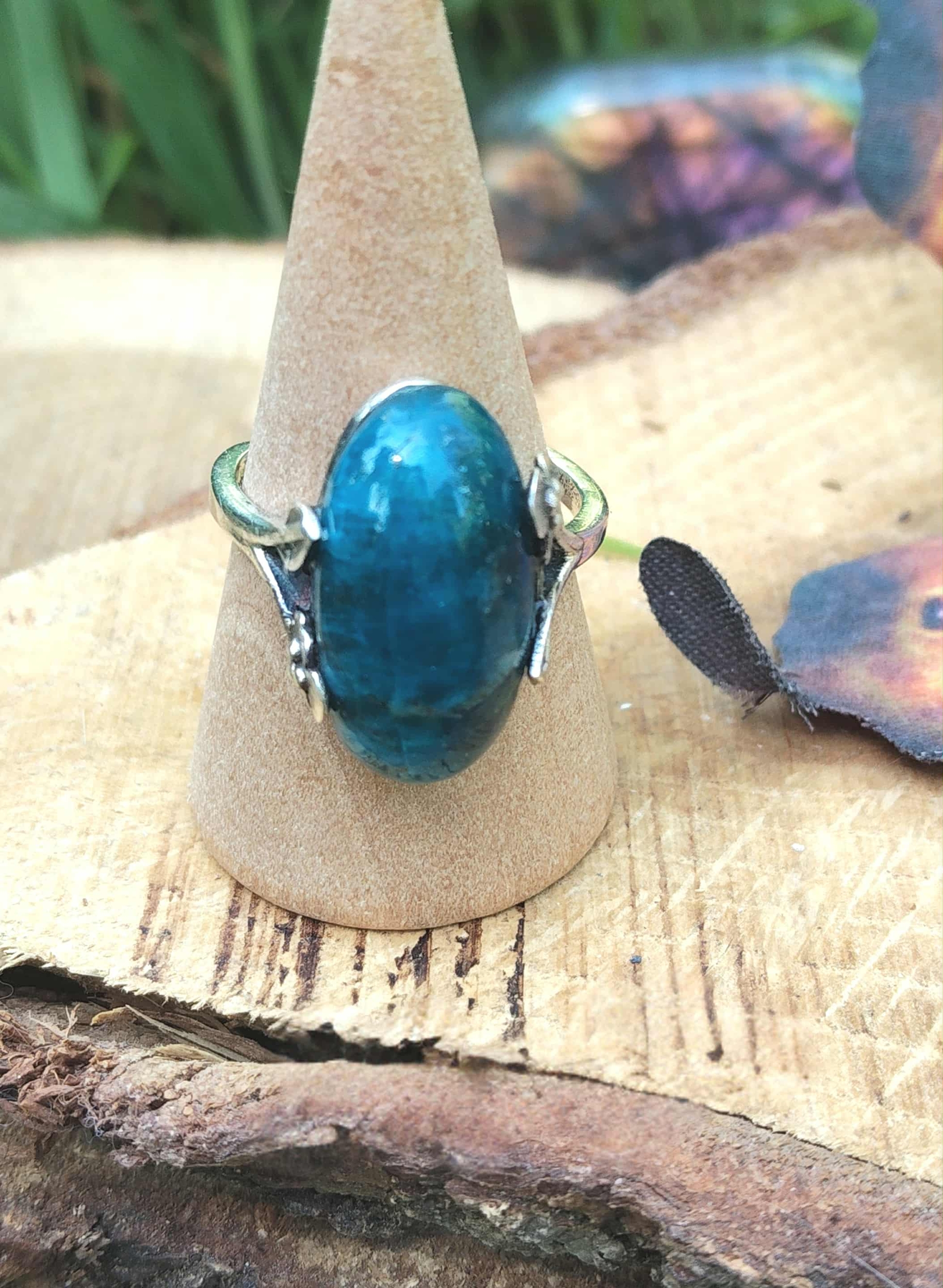 Bague apatite bleue réglable en argent 925 sur cône bois, posée sur rondin ; papillon flou à droite — communication, clarté mentale, équilibre émotionnel