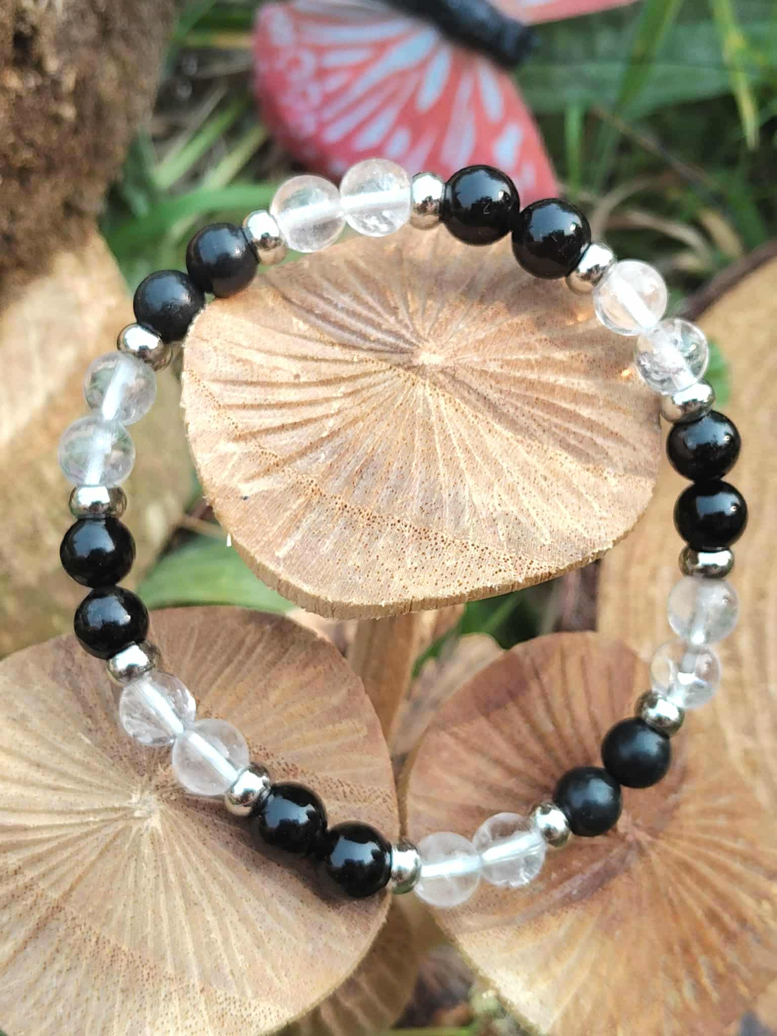 Bracelet protection en shungite, tourmaline noire et cristal de roche — cercle posé sur chapeaux de champignons beiges, décor naturel avec papillon en arrière plan