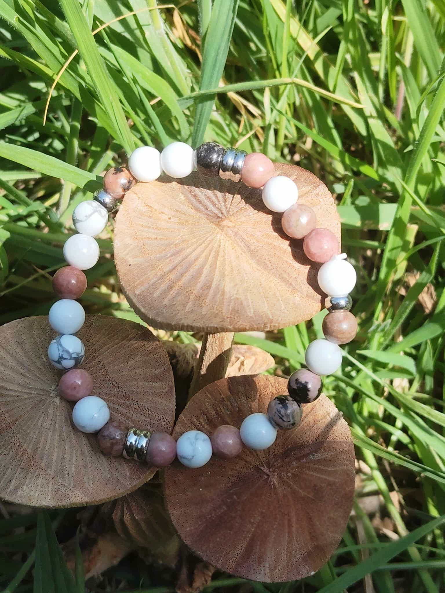 Bracelet howlite et rhodonite sur champignons de bois dans l’herbe, apaisement émotionnel et travail symbolique sur l’enfant intérieur