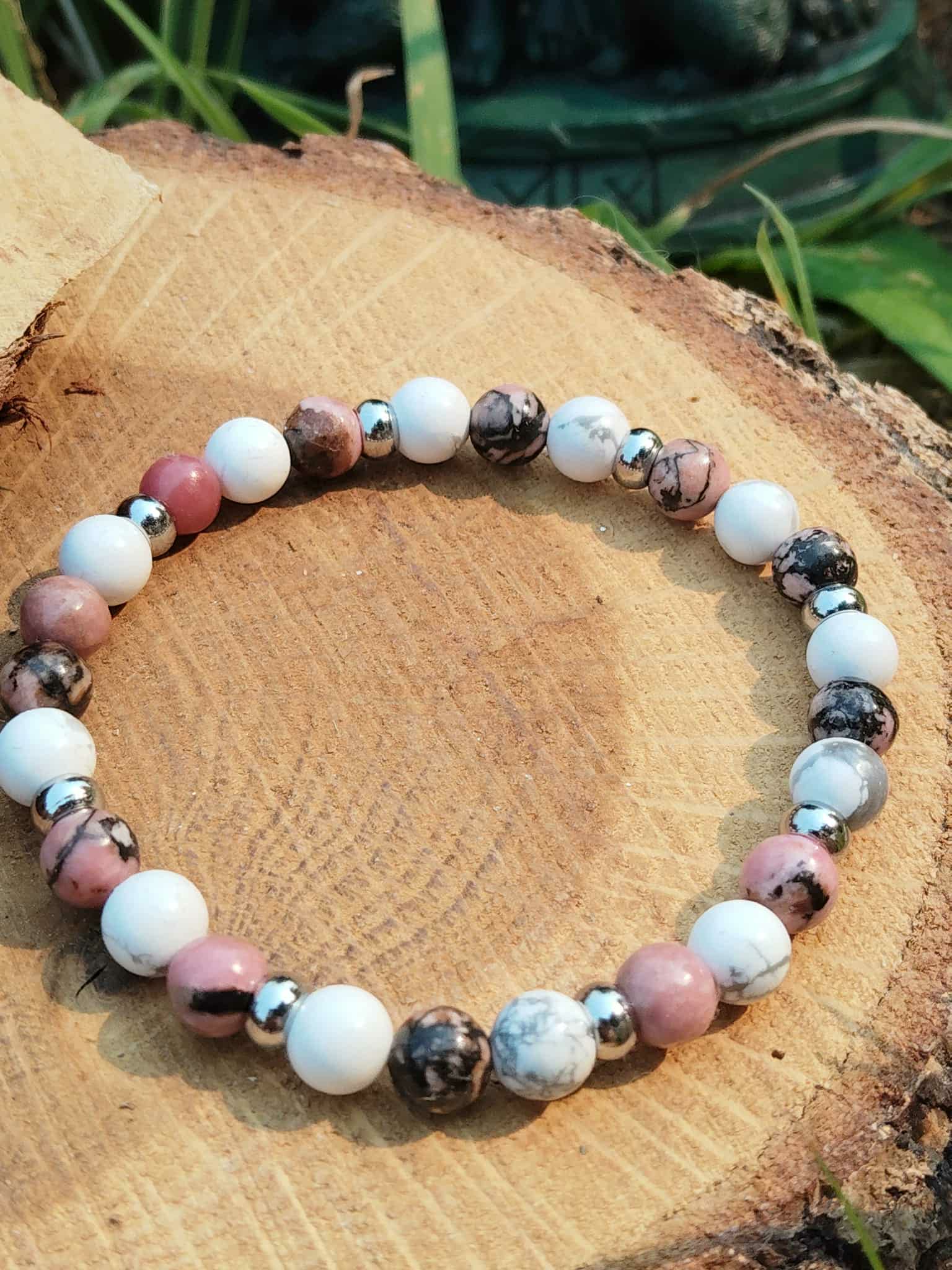Bracelet howlite et rhodonite sur rondin avec fond végétal, recentrage émotionnel, stabilité intérieure et énergie plus douce