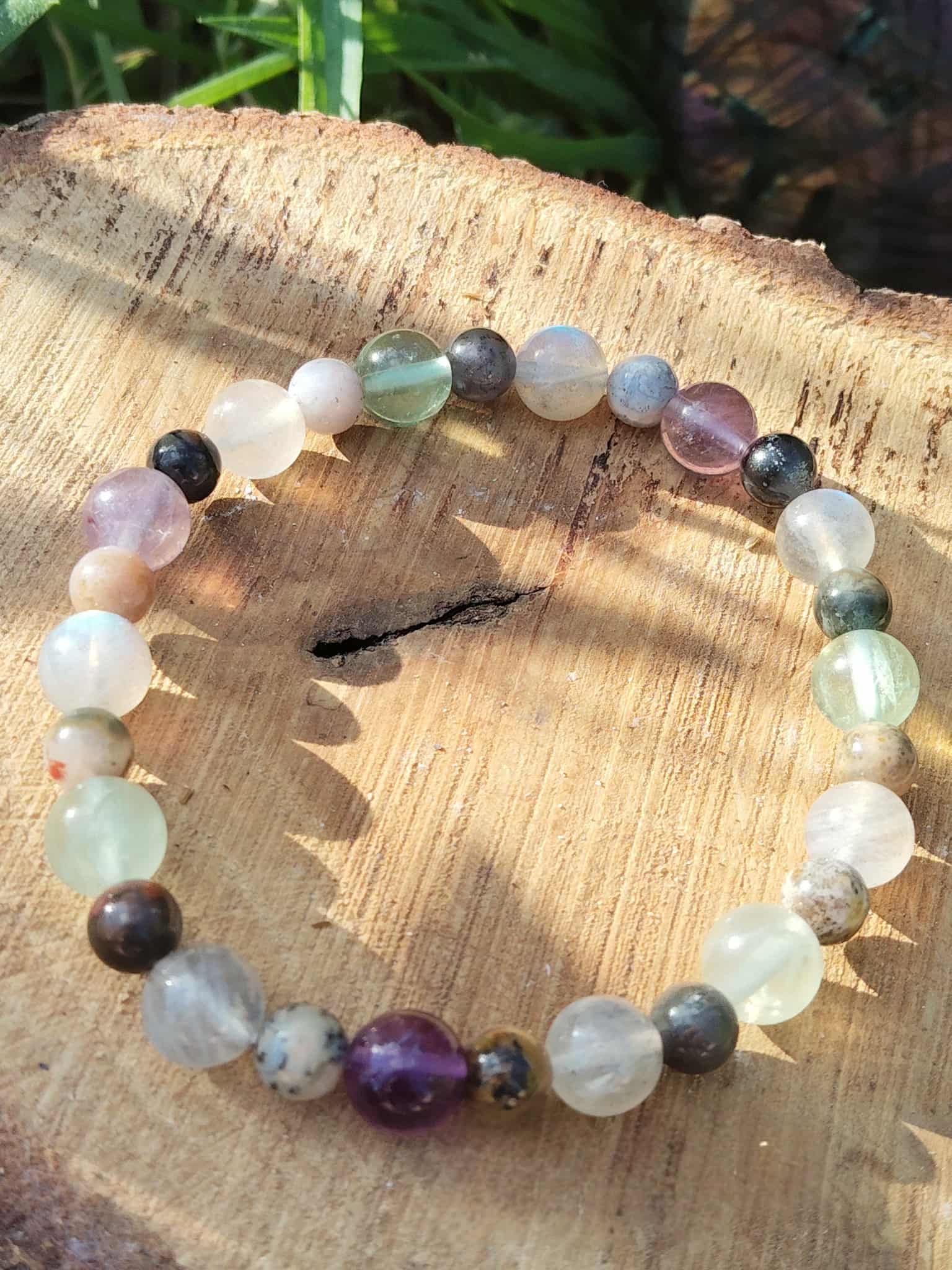 Bracelet troisième œil posé sur rondin de bois en extérieur, herbe en arrière-plan, exploration spirituelle et connexion aux vies antérieures