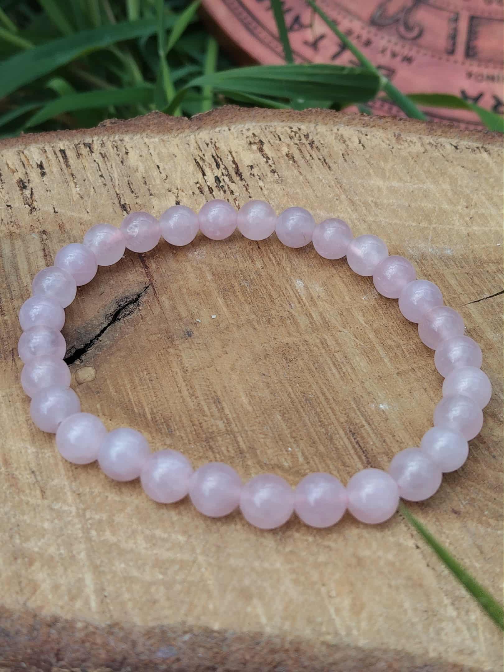 Bracelet quartz rose 6 mm posé sur support en bois, délicatesse émotionnelle, harmonie du cœur et sérénité affective