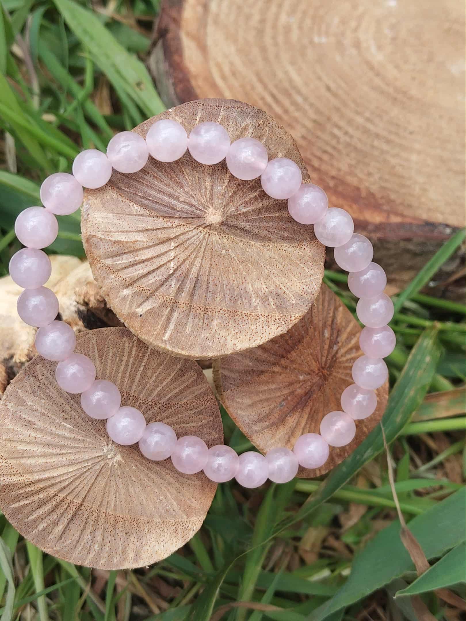 Bracelet quartz rose en perles rondes sur champignons décoratifs dans l’herbe, bienveillance, sensibilité apaisée et tendresse relationnelle